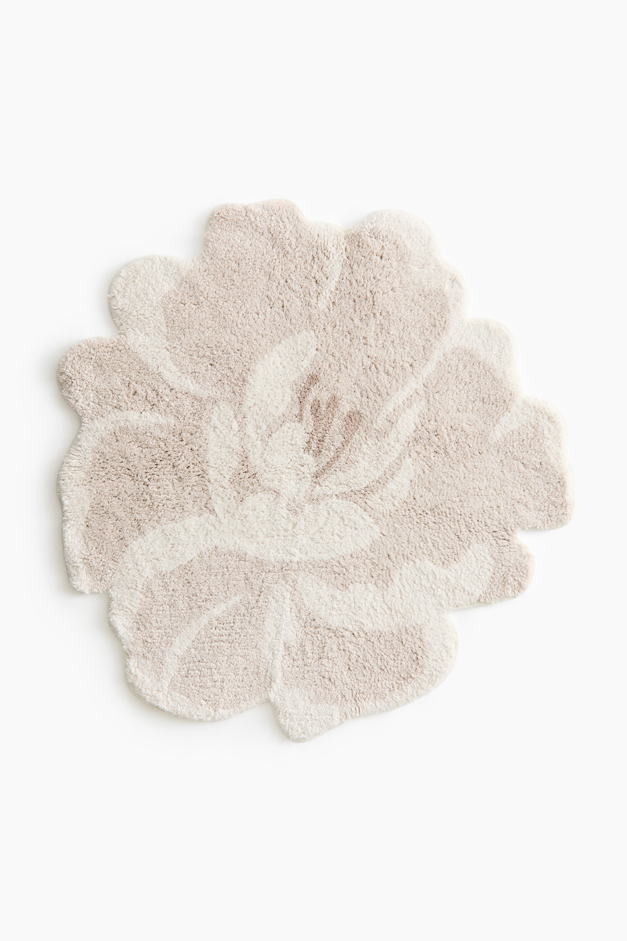 View larger image: A flower-shaped rug, viewed from the front, features a soft, plush tufted pile with a stylised floral design. The pattern uses varying pile heights in shades of cream and light beige to define the textured petals and central stamen.