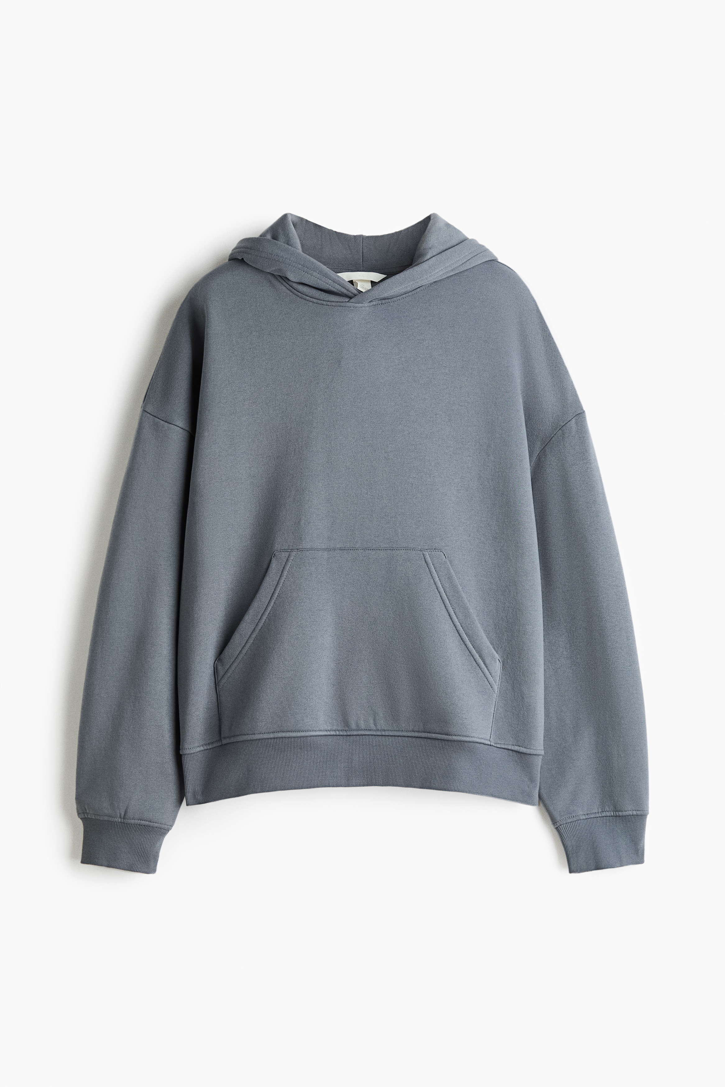 A gray sweat fabric hoodie featuring a double-layer hood, dropped shoulders, and a kangaroo pocket is being worn by the model. The model is adjusting the collar of the hoodie, which is styled with matching wide-leg sweatpants and a white underlayer visible at the neck and cuffs.