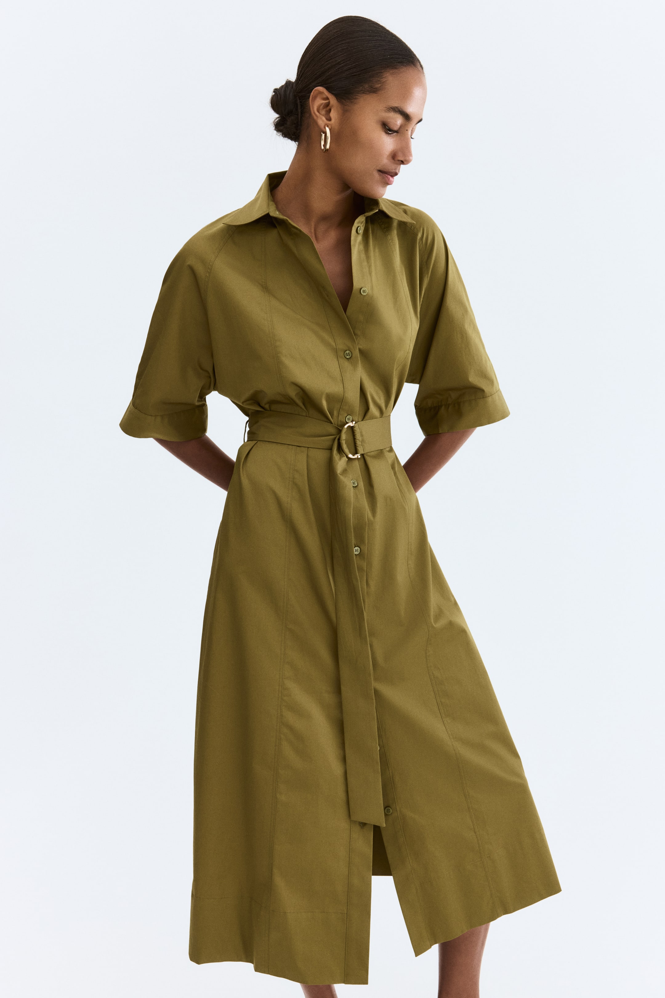 View larger image: An olive green shirt dress, slightly angled to the right, features a pointed collar, a button-down front, and wide short sleeves. A matching fabric belt with a gold-tone D-ring buckle cinches the waist, and its A-line skirt falls to a midi length with side slits.