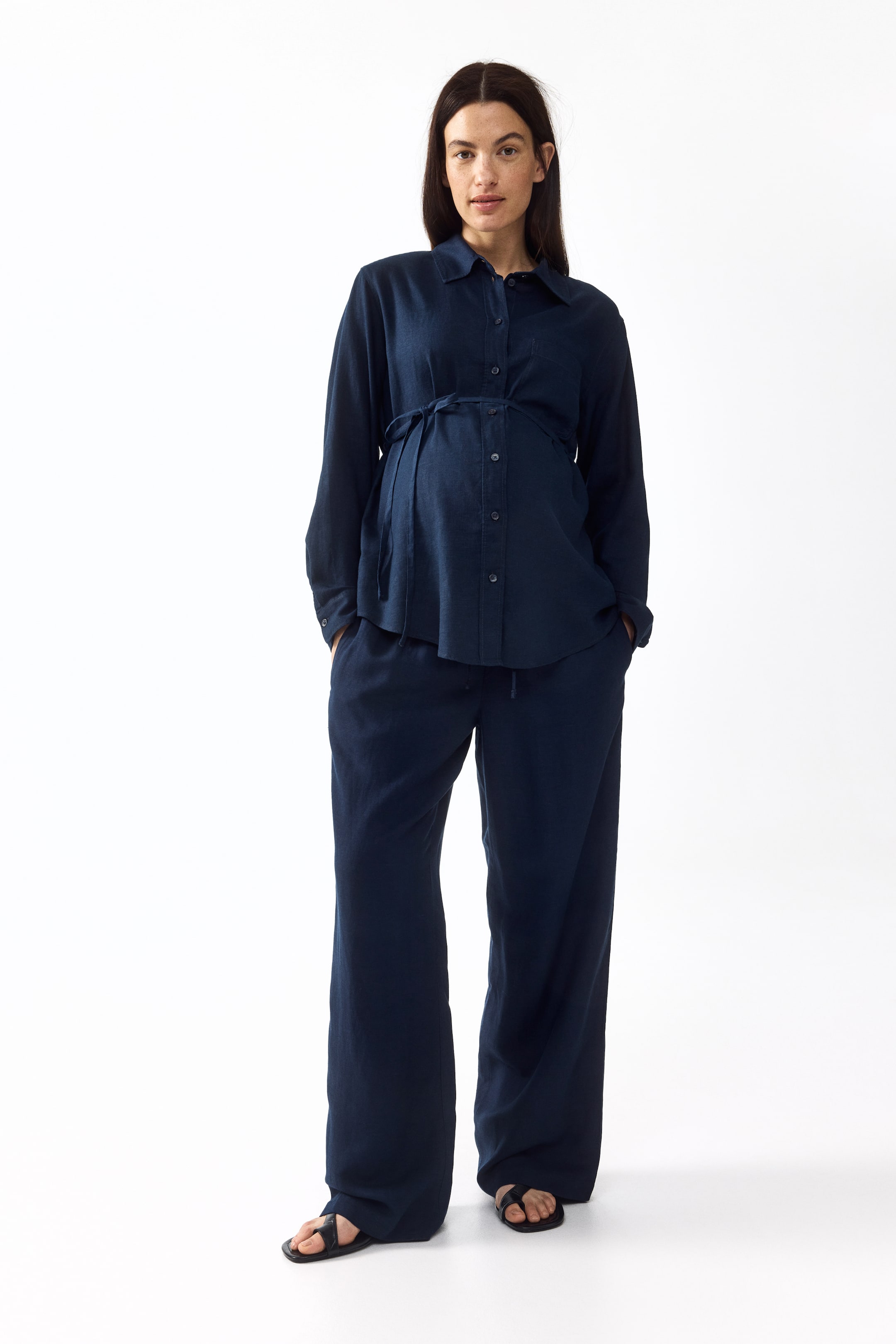 View larger image: A navy blue two-piece set features a collared, long-sleeved button-down shirt and wide-leg trousers, displayed from the front. The shirt cinches at the waist with a drawstring tie, creating a gathered effect, and the trousers exhibit a relaxed fit with a drawstring waist.