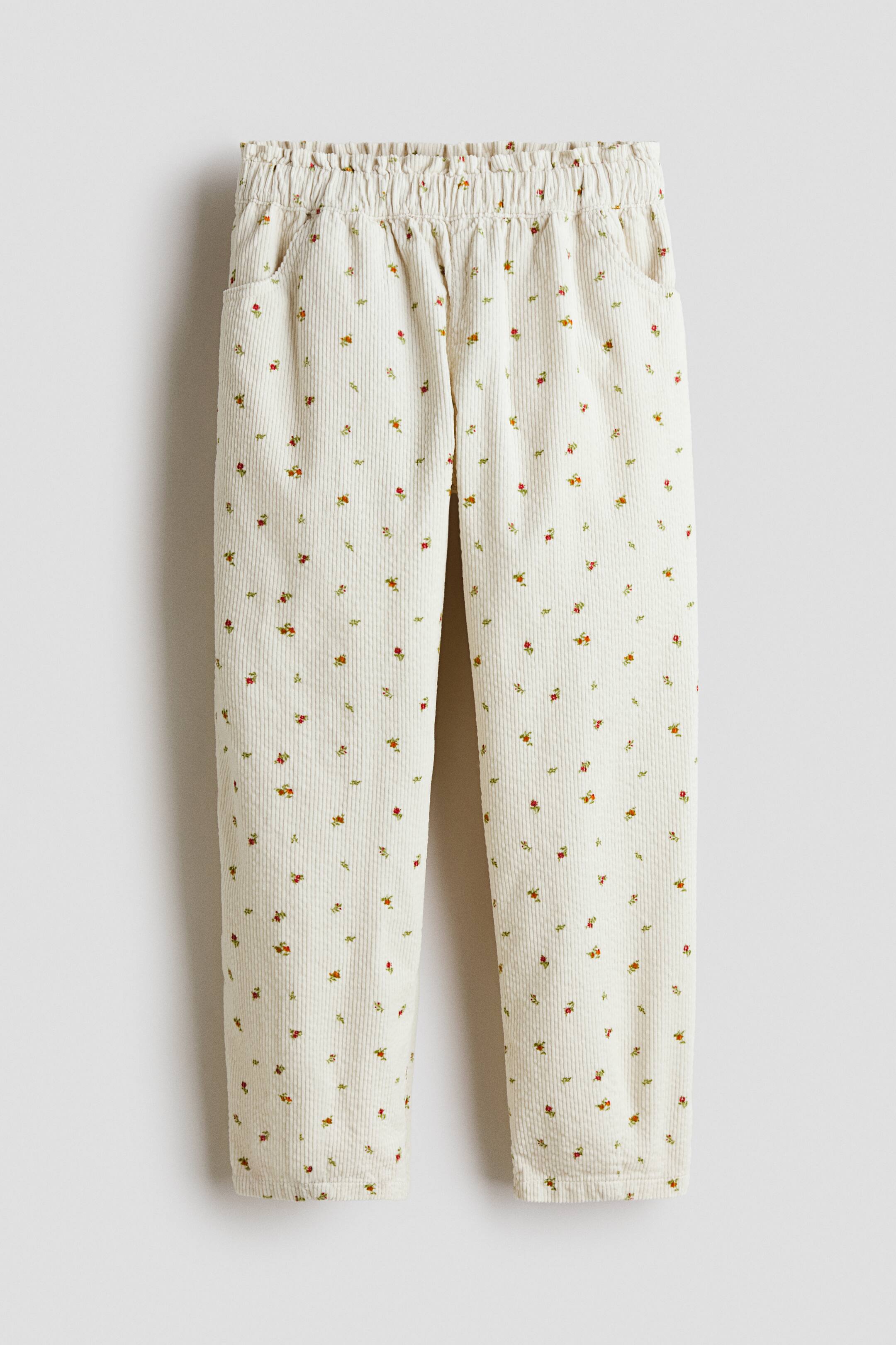 Voir une image plus grande: Le pantalon est présenté à plat, face vers l’avant, dans un tissu en velours côtelé crème orné d’un motif dispersé de petites fleurs rouges et vertes. Il est doté d’une taille élastiquée froncée et de deux poches avant visibles.