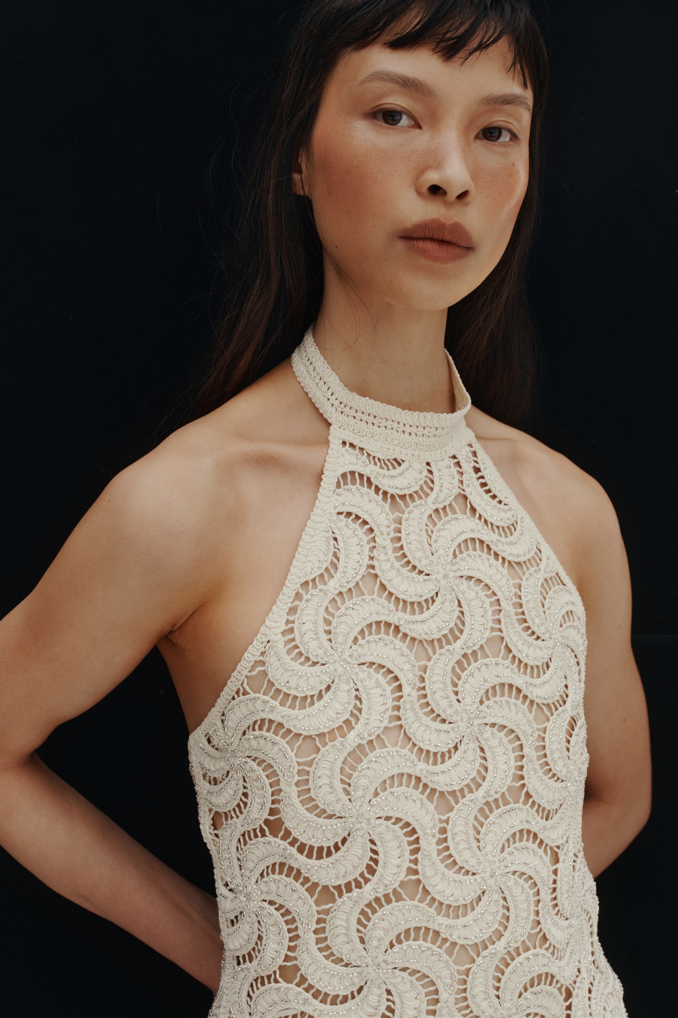 Voir une image plus grande: Le modèle porte un haut dos nu crème. Il est confectionné dans un tricot à l'allure crochet, avec un motif tourbillonnant et des perles métalliques scintillantes sur le devant, et présente une coupe étroite au niveau du cou.