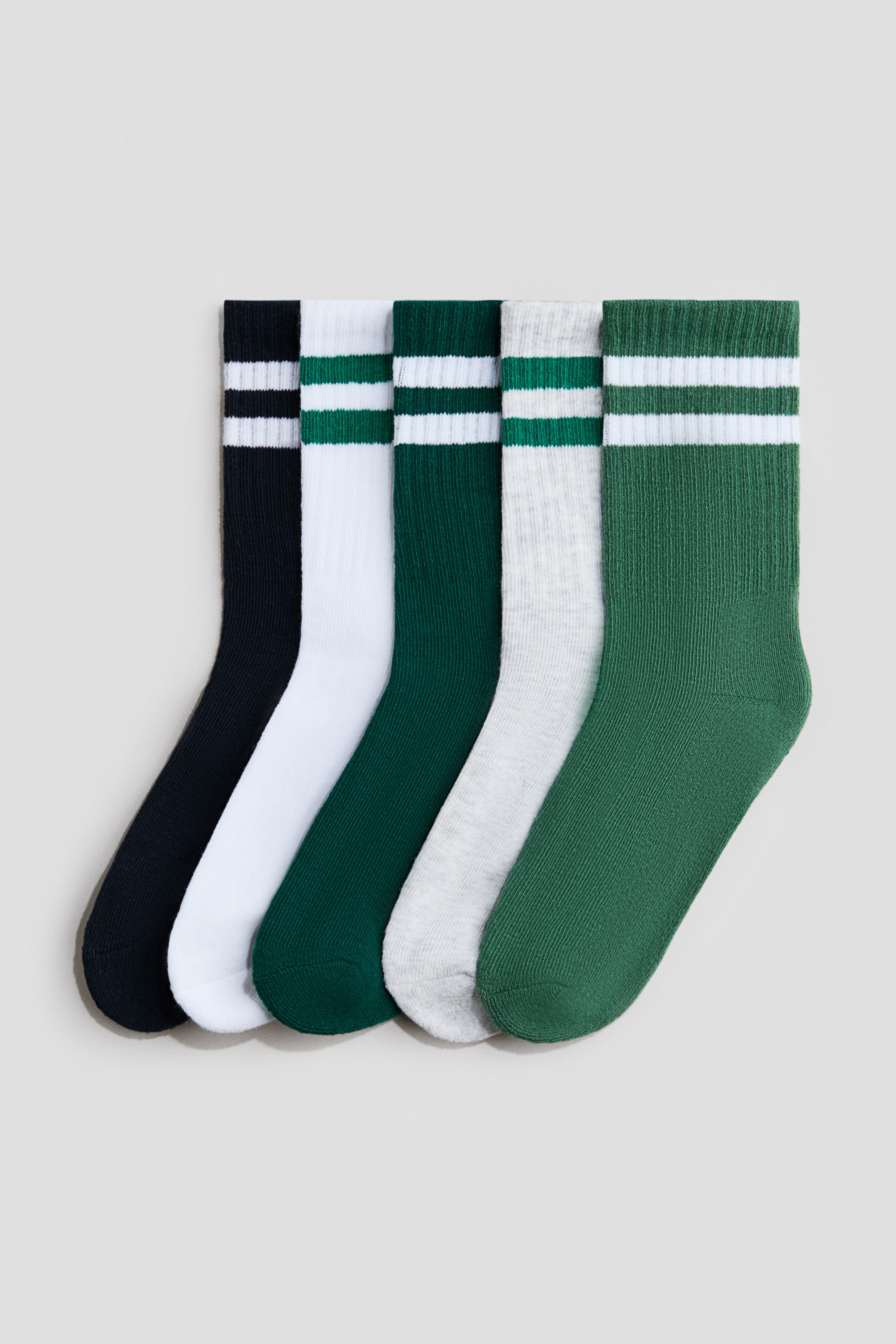 View larger image: Five pairs of socks are displayed at the forefront, fanning out from left to right, each showcasing ribbed shafts. Four pairs boast two horizontal stripes: black with white, white with green, dark green with white, and light grey heather with green, while the fifth pair is a solid dark green.