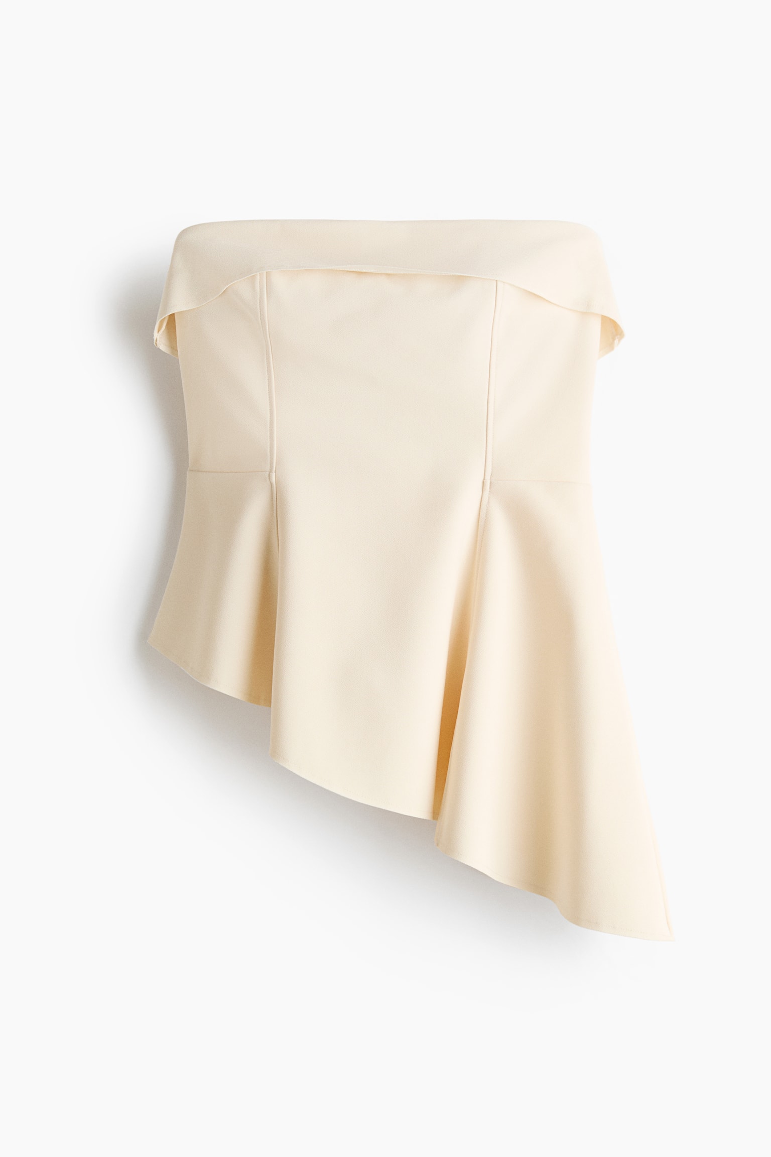 A cream strapless top is shown from the front, featuring a structured bodice with vertical seams and a fold-over band at the neckline. The top flows into an asymmetrical, draped peplum hemline, longer on the right-hand side.