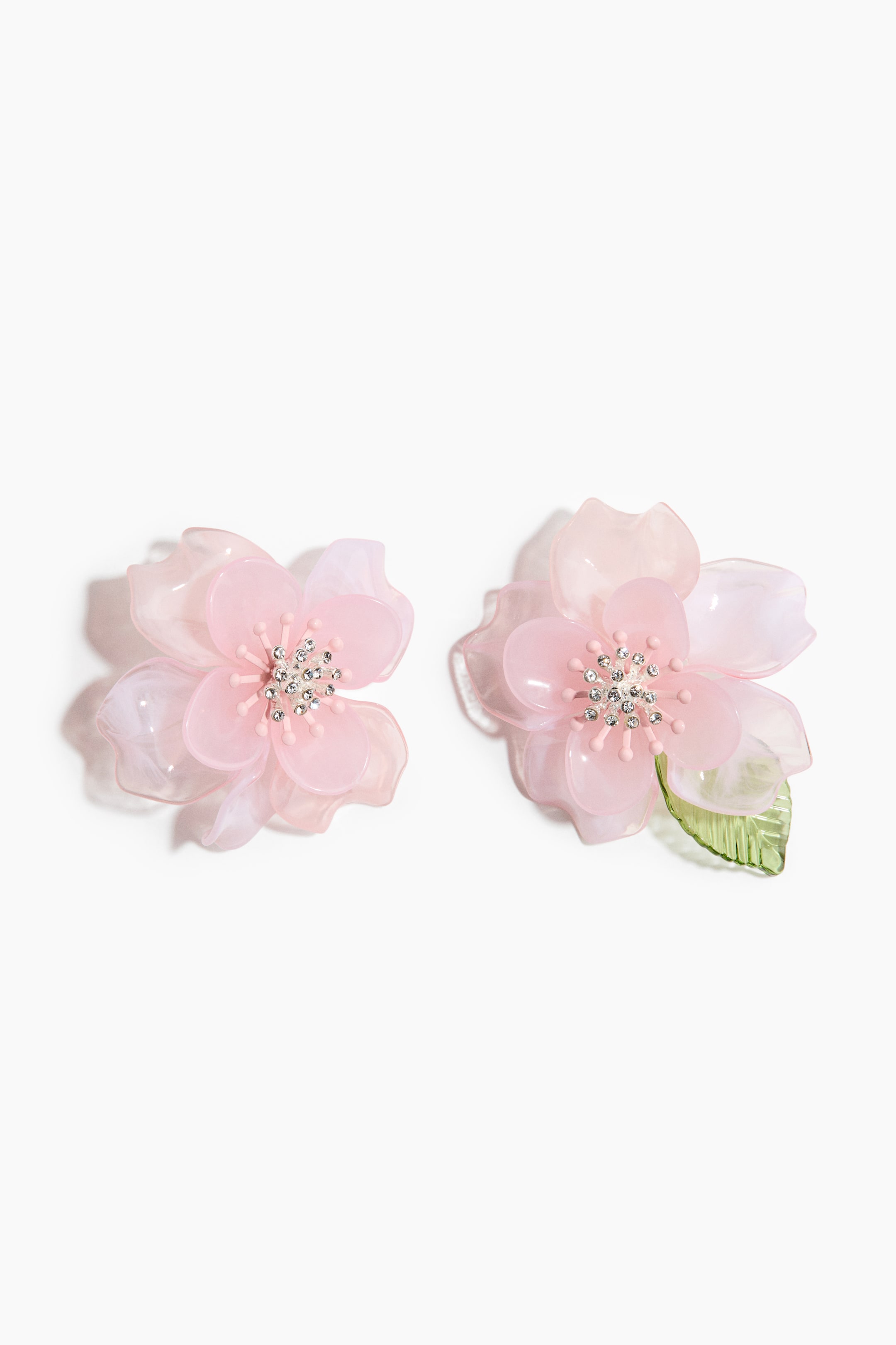 View larger image: Two floral earrings are showcasing translucent pink layered petals, with each earring featuring a centre embellished with pink stamen-like elements and clear sparkling stones. The earring on the right is also displaying a translucent green leaf.