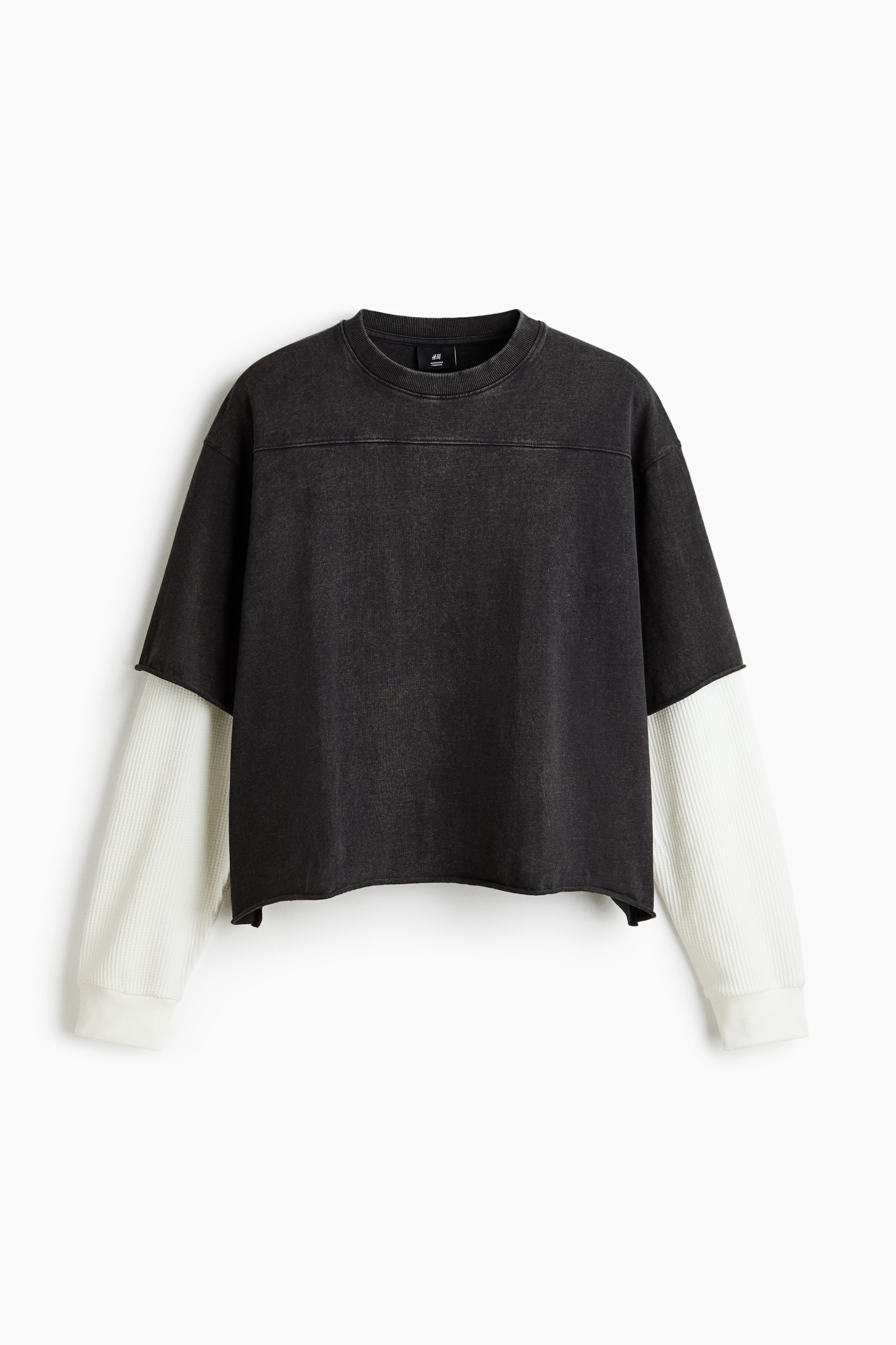 Voir une image plus grande: Un chandail noir délavé est présenté de face, mettant en valeur un design superposé. Il comprend une couche supérieure noire à manches courtes avec un col rond, une couture horizontale sur la poitrine et un ourlet à coupe brute, recouvrant de longues manches blanches côtelées avec poignets côtelés.