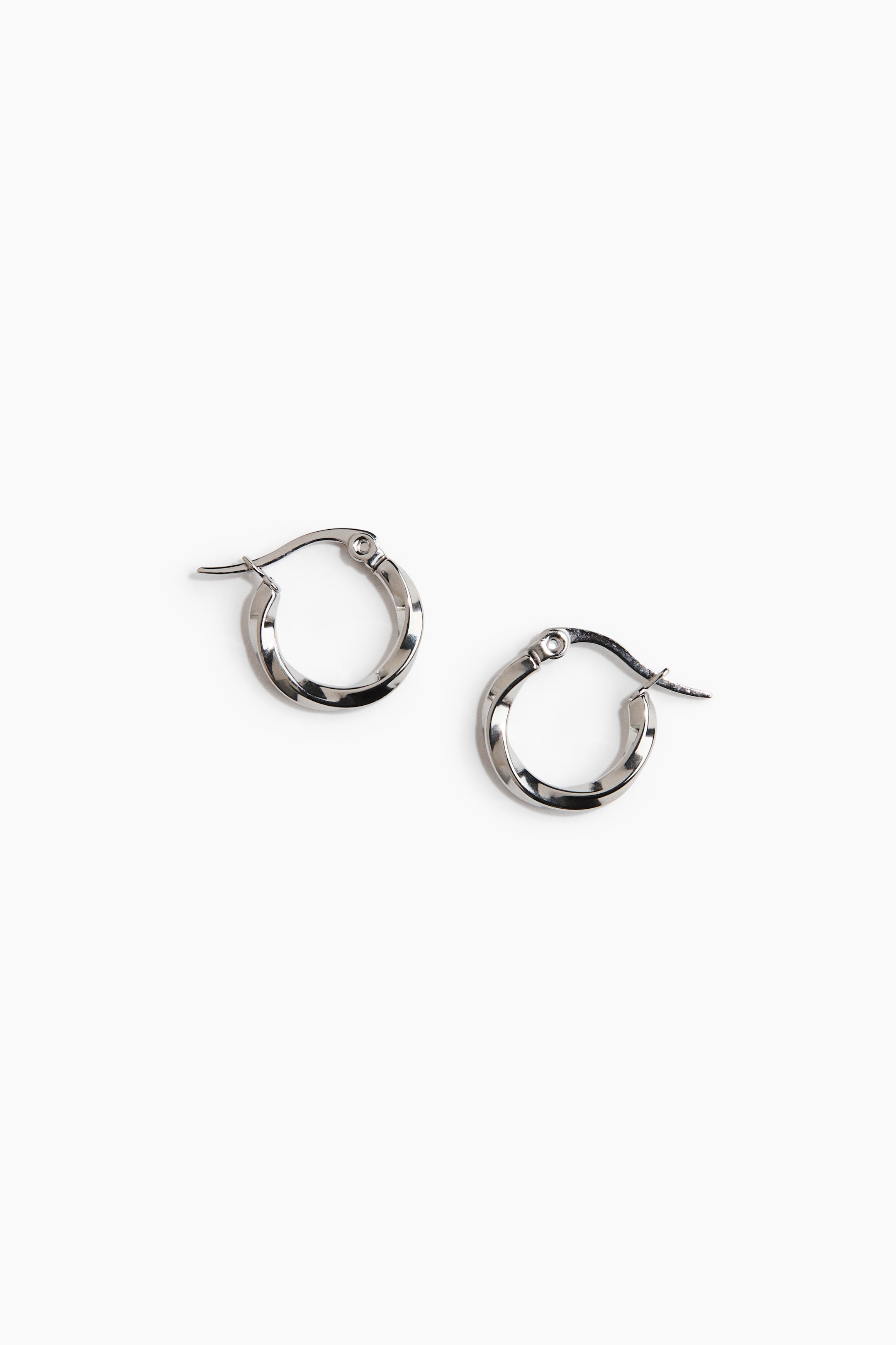 View larger image: Two polished silver-toned hoop earrings lie flat, each boasting a faceted, twisted surface. Each earring features a hinged post closure.