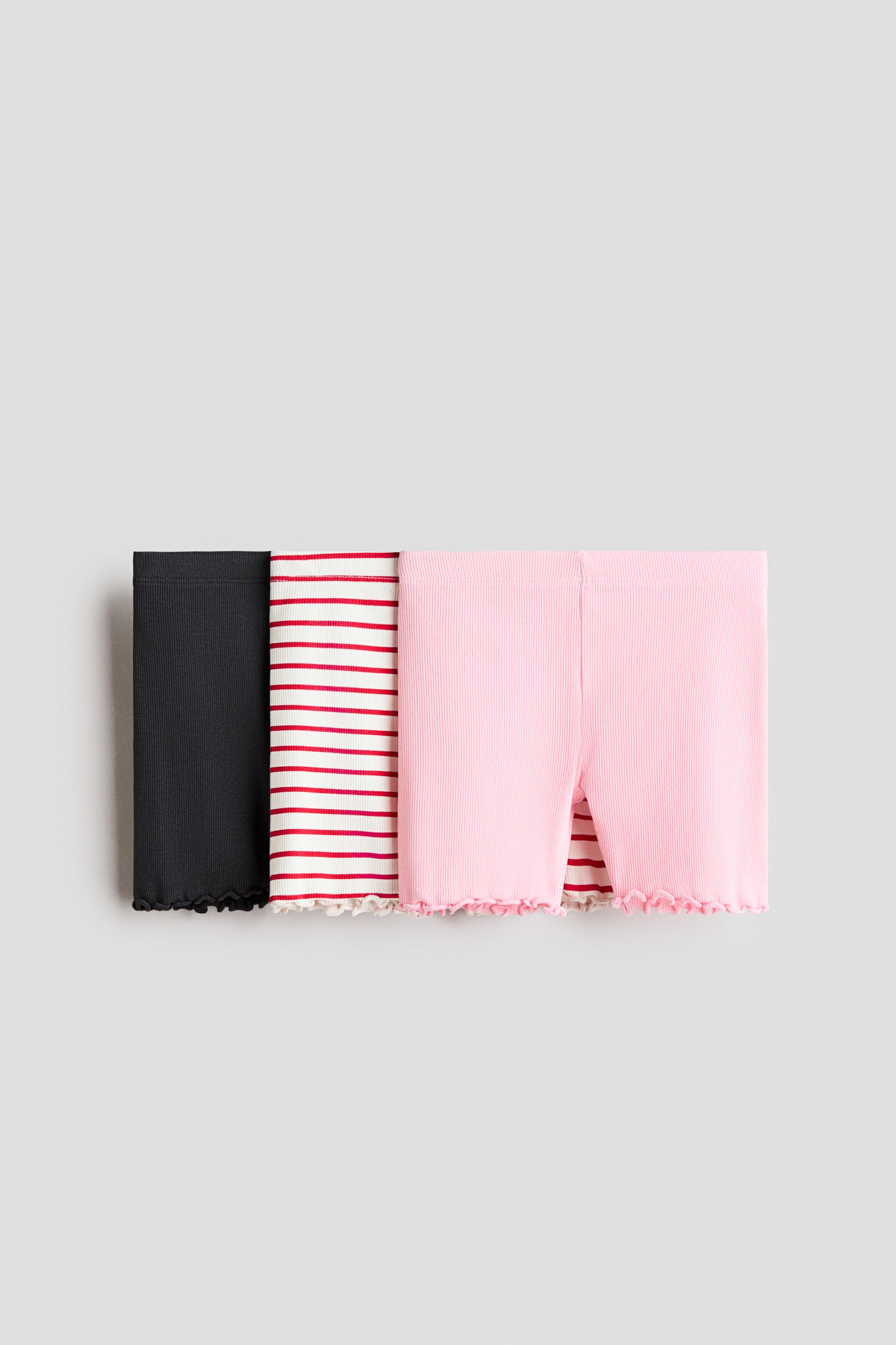 View larger image: Three pairs of cycling shorts shown from the front display ribbed cotton jersey, elastic waistbands, and overlocked trims on the hems. The shorts are shown in black, white with red horizontal stripes, and pink.