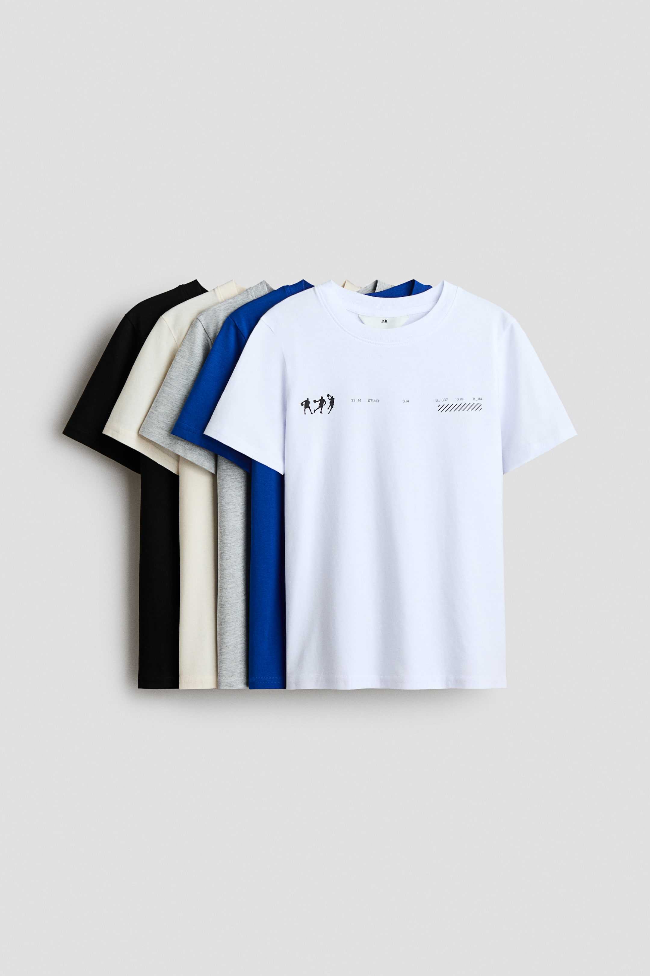 View larger image: T-shirts made from soft cotton jersey are arranged in a fan-like display, showcasing an array of designs and colors such as black, light beige, grey, blue, and white. The foremost white t-shirt features a graphic design with black figures and text, and all t-shirts are styled with a round, rib-trimmed neckline.