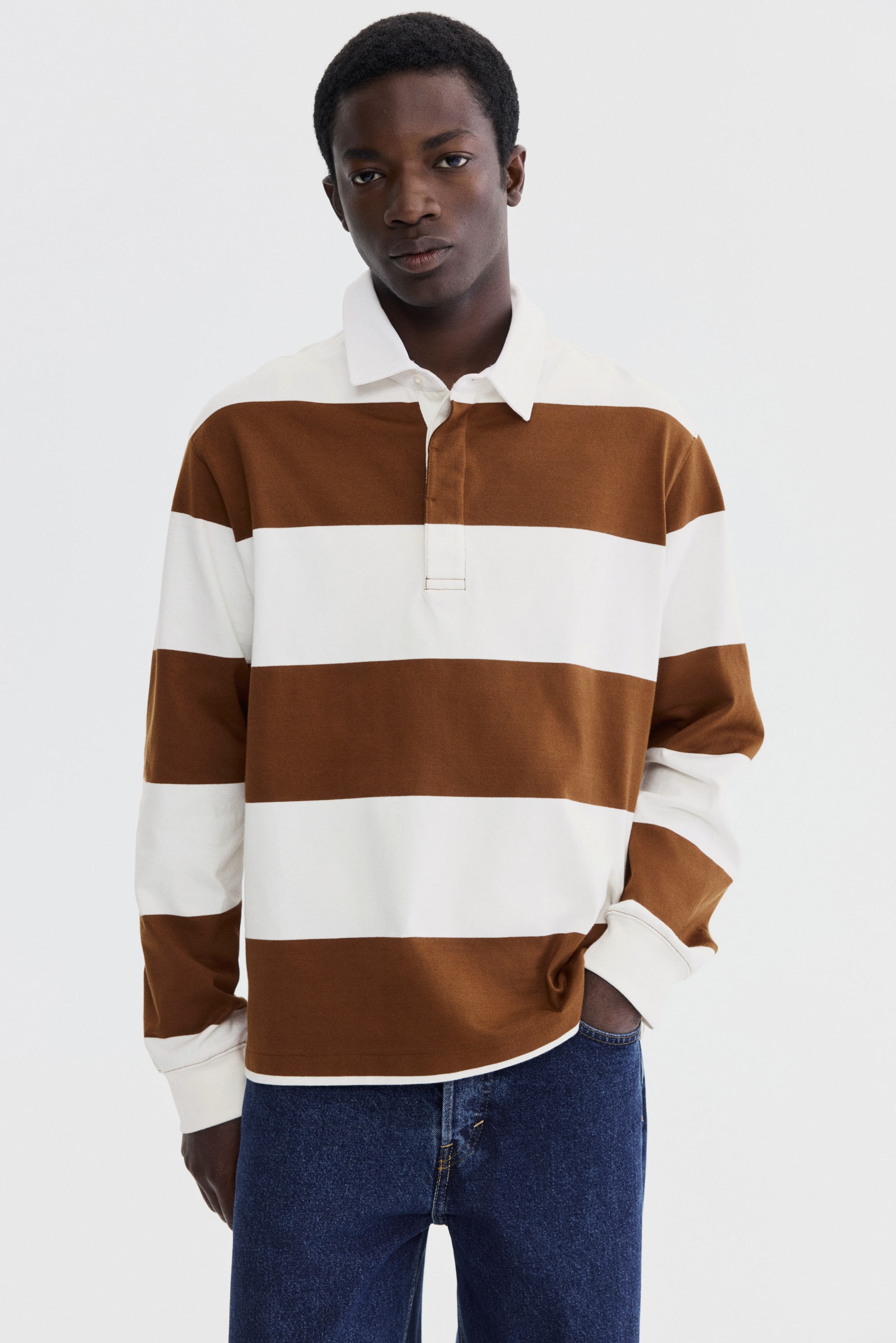 View larger image: A long-sleeved polo shirt showcasing horizontal brown and white stripes, complemented by a white spread collar and a white placket with two visible buttons. Its long sleeves culminate in plain cuffs, and it is presented facing forward.