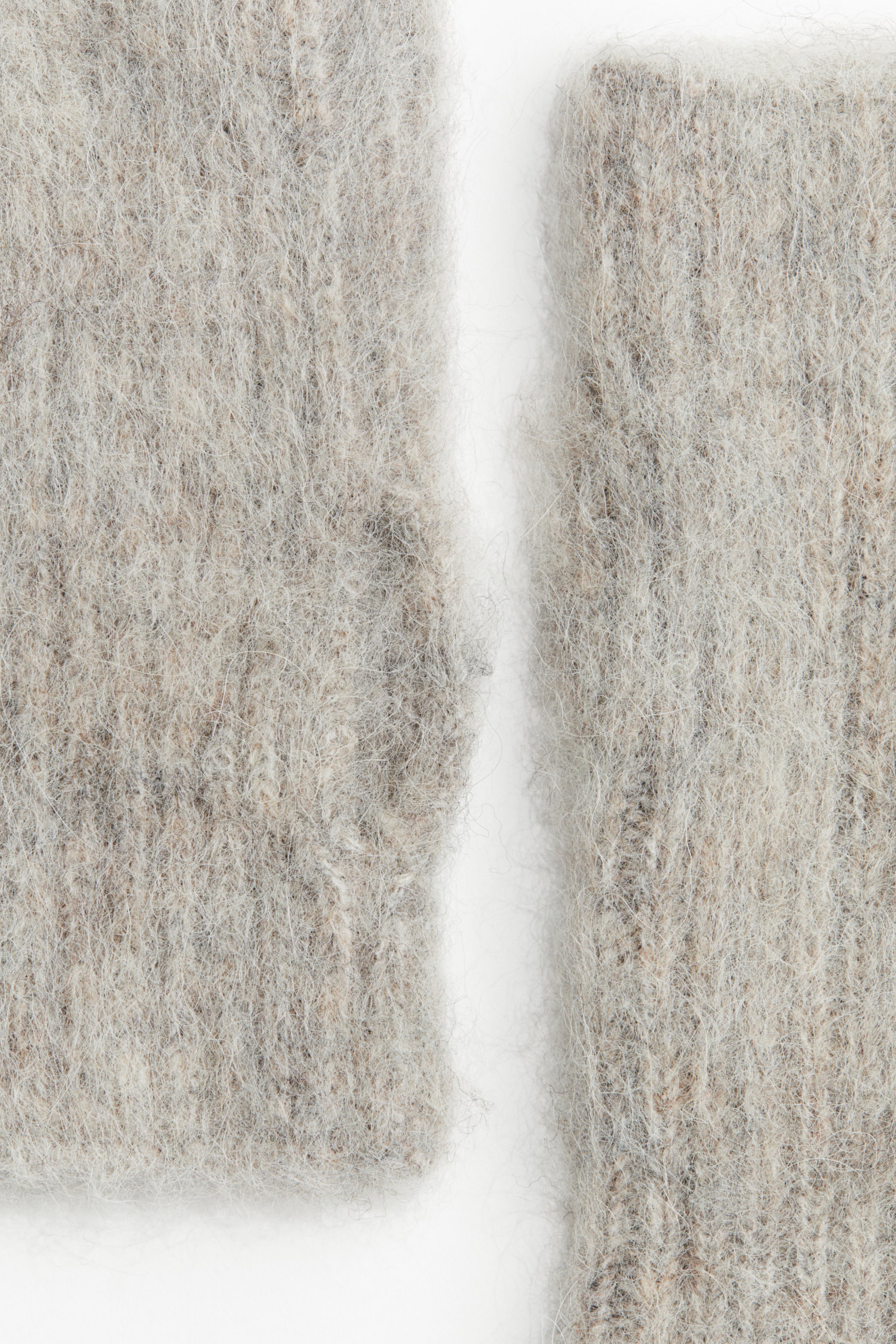 拡大画像を表示: 一対のリストウォーマーは、ライトグレーとベージュの柔らかいニットが特徴です。生地は、目に見える繊維で目立つふわふわした質感を示しています。
