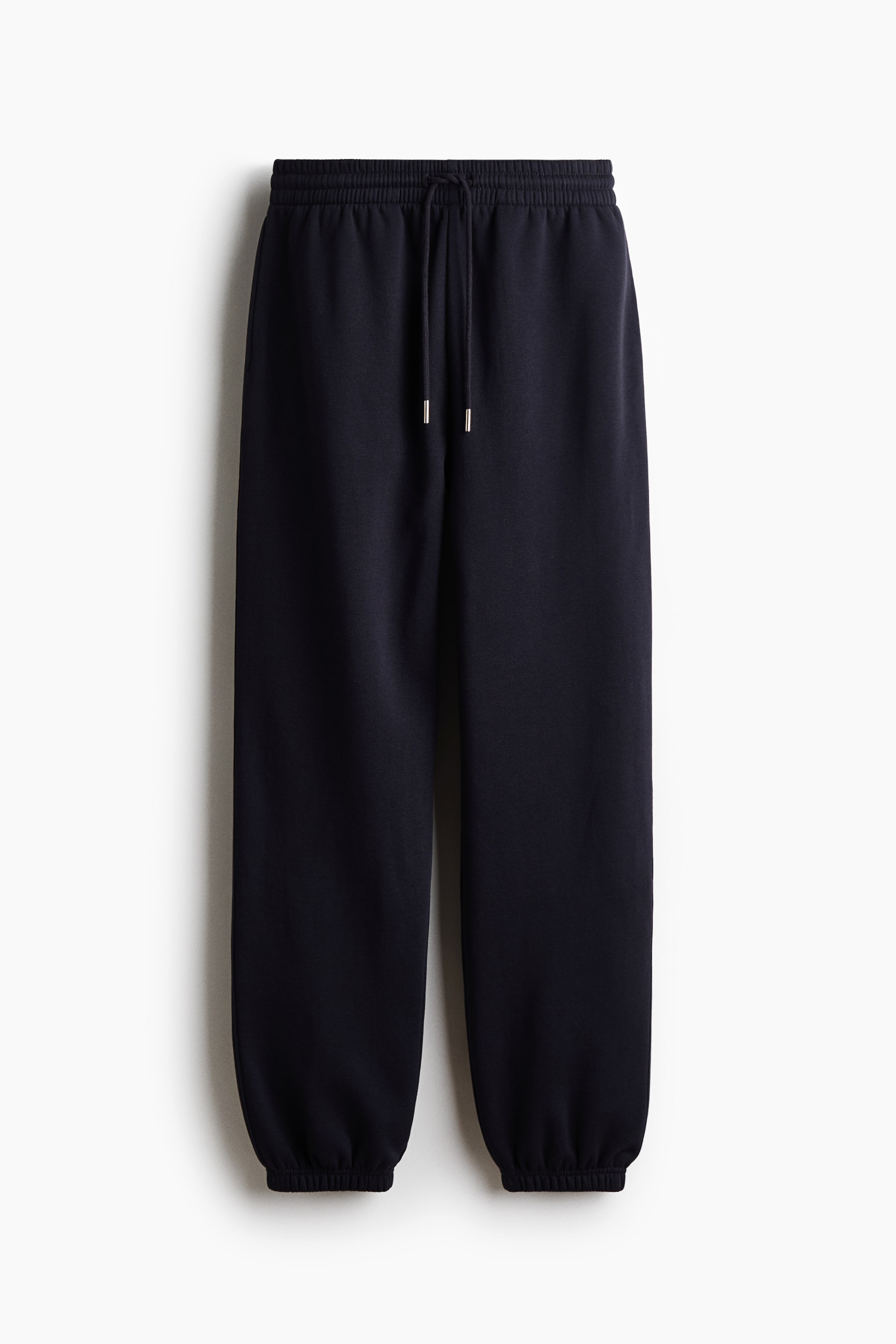View larger image: A pair of dark navy blue track pants is shown from the front, featuring a high, covered elastic waistband with an adjustable drawstring. The design showcases a relaxed leg fit with side pockets and gathered elastic cuffs at the hems.