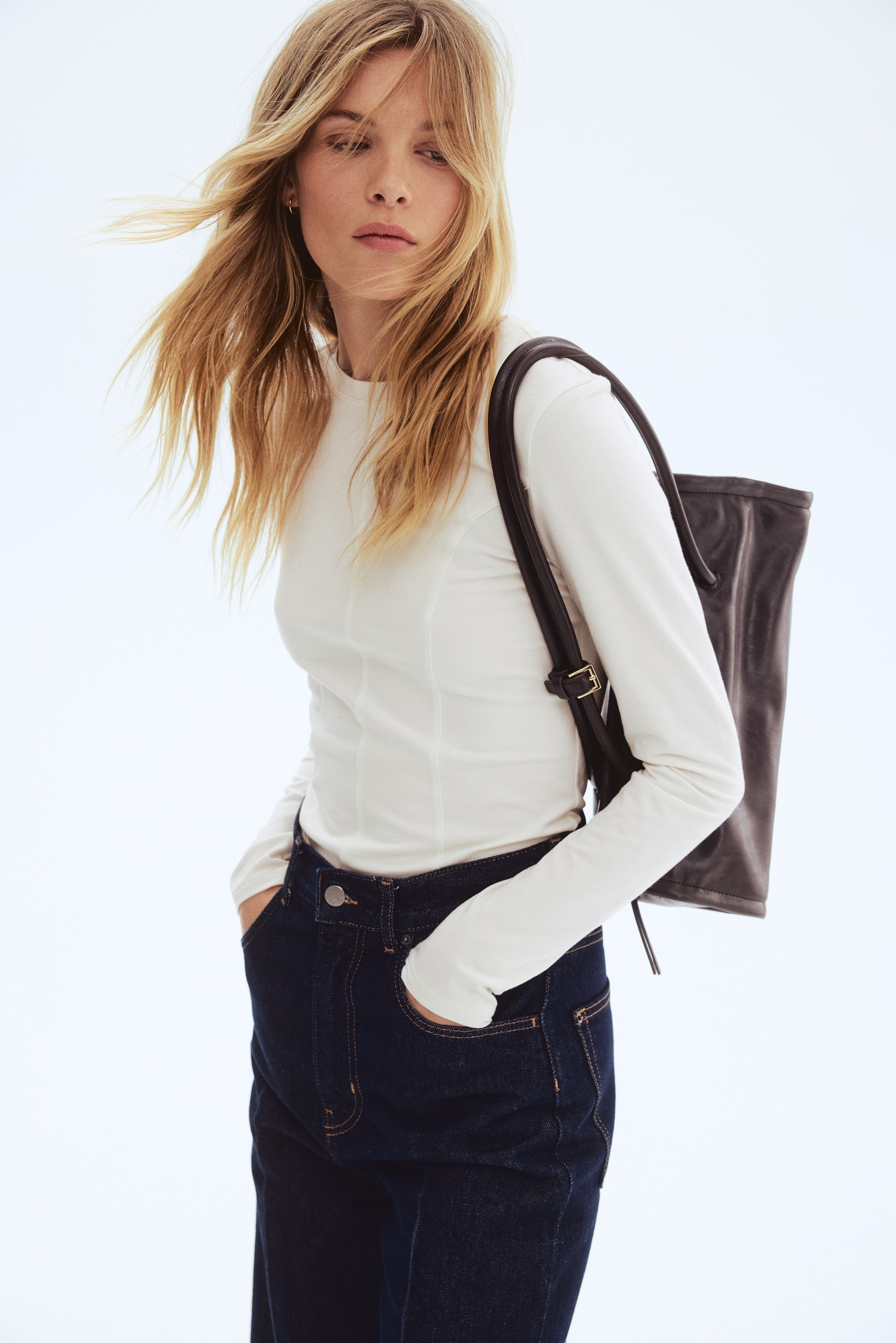 Agrandir l'image: Un haut à manches longues blanc est présenté de face, légèrement incliné. Il se caractérise par un col rond, des manches longues et des détails de coutures verticales qui épousent le torse, et est porté rentré dans un jean bleu foncé.