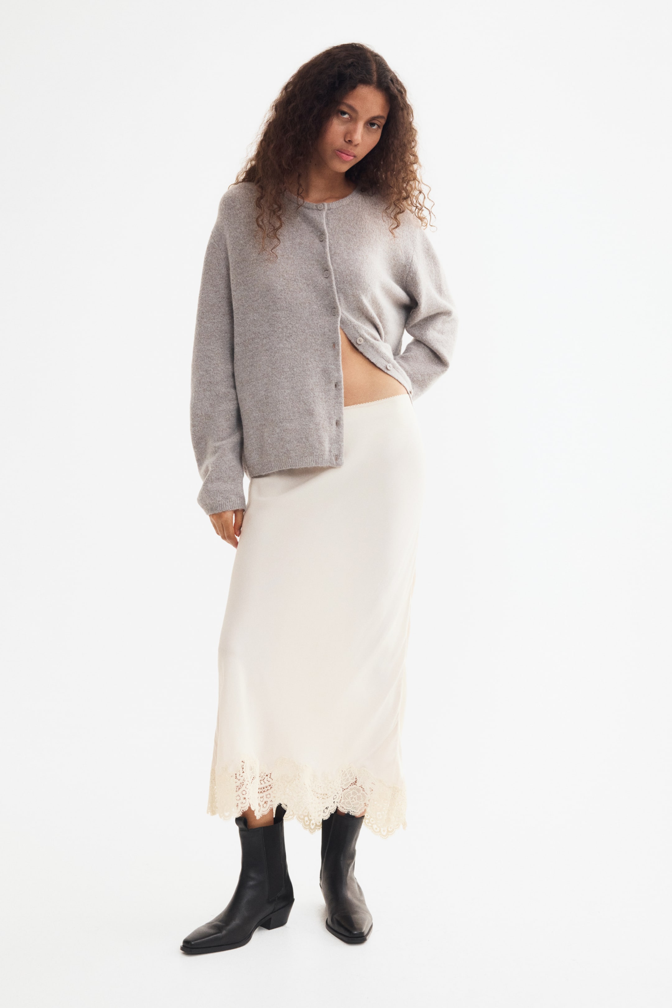 View larger image: The model is wearing a cream, calf-length skirt in a light viscose weave. The skirt features a scalloped lace trim at the hem and is styled with black boots.