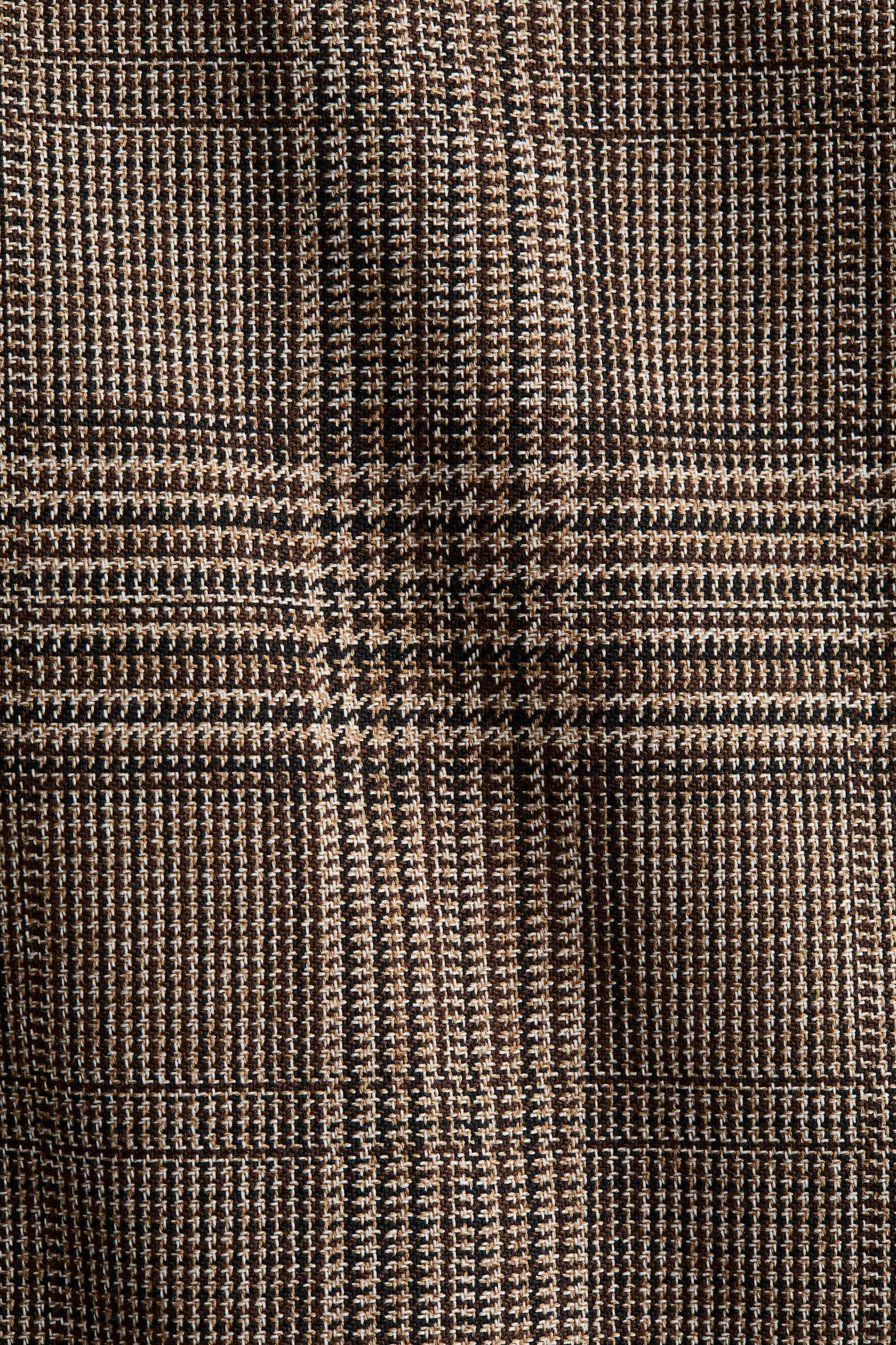 View larger image: The fabric is presenting a Glen plaid pattern, featuring a woven texture in shades of brown, black, and beige.