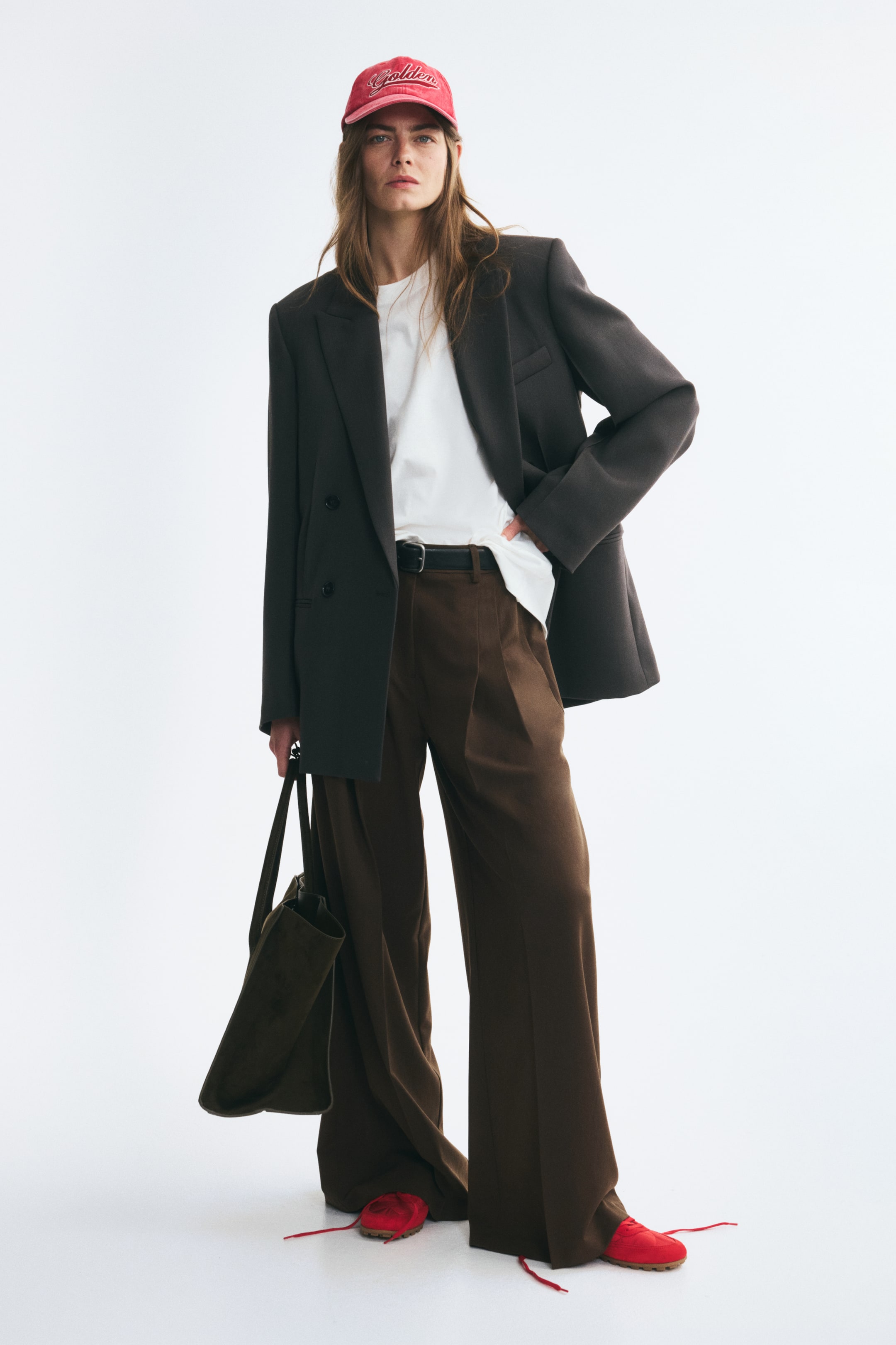 Ampliar la imagen: La modelo lleva pantalones color café de corte holgado en tejido plano, con piernas amplias, pinzas al frente, marcado de raya y un cinturón negro. Los pantalones se combinan con una camiseta blanca parcialmente metida por dentro y un blazer oscuro oversize.