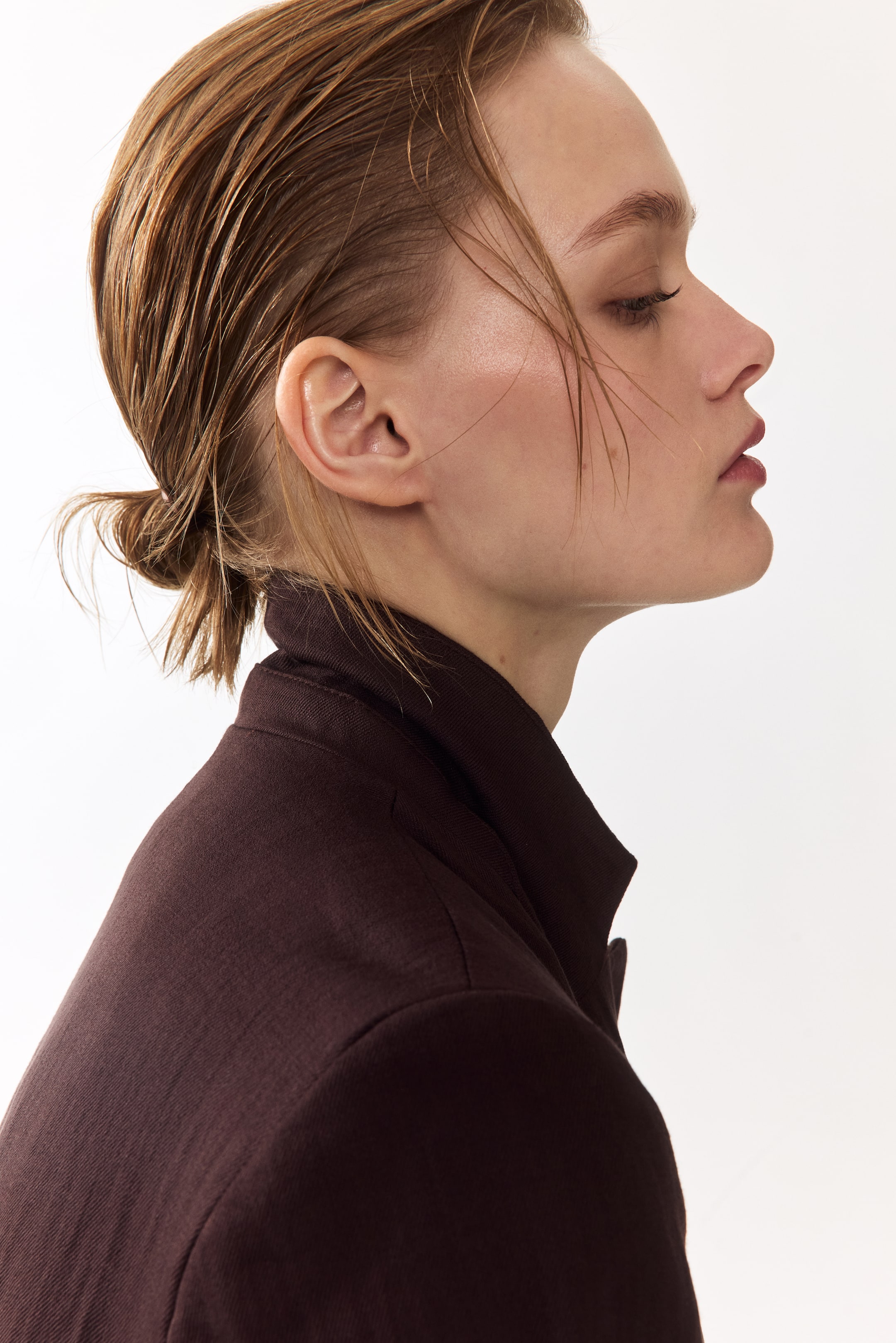 Ver imagen más grande: Se presenta una chaqueta marrón oscuro de perfil lateral, con un cuello alto estructurado alrededor del cuello. La tela texturizada de la chaqueta y la costura del hombro entallada son visibles, mostrando su confección.