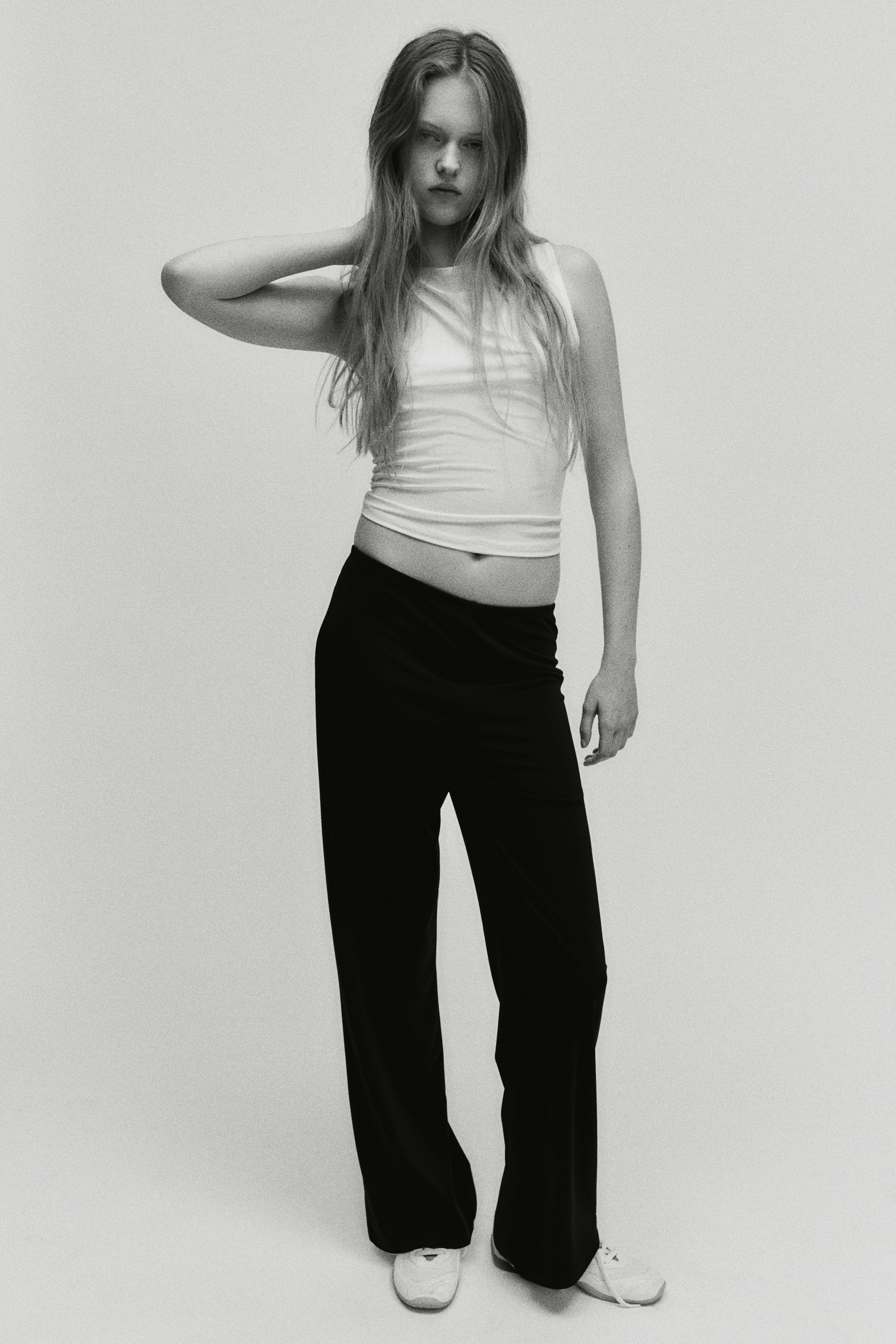 View larger image: The model is wearing a fitted, slightly cropped white sleeveless top paired with black wide-leg pants.