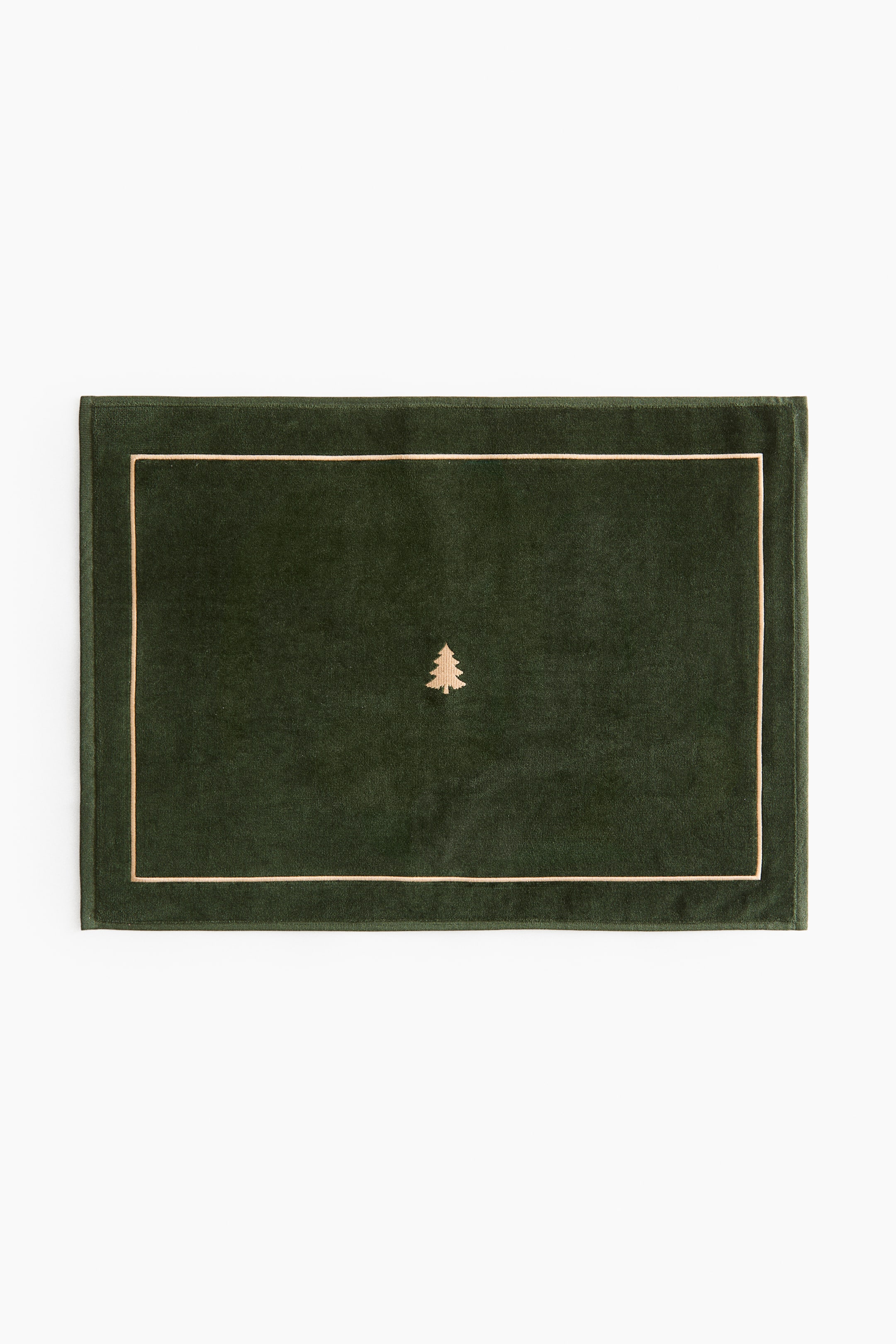 View larger image: A rectangular dark green velour bath mat is shown from the front, featuring a light gold satin-stitched border around the edges and a small light gold embroidered evergreen tree centered on the surface.