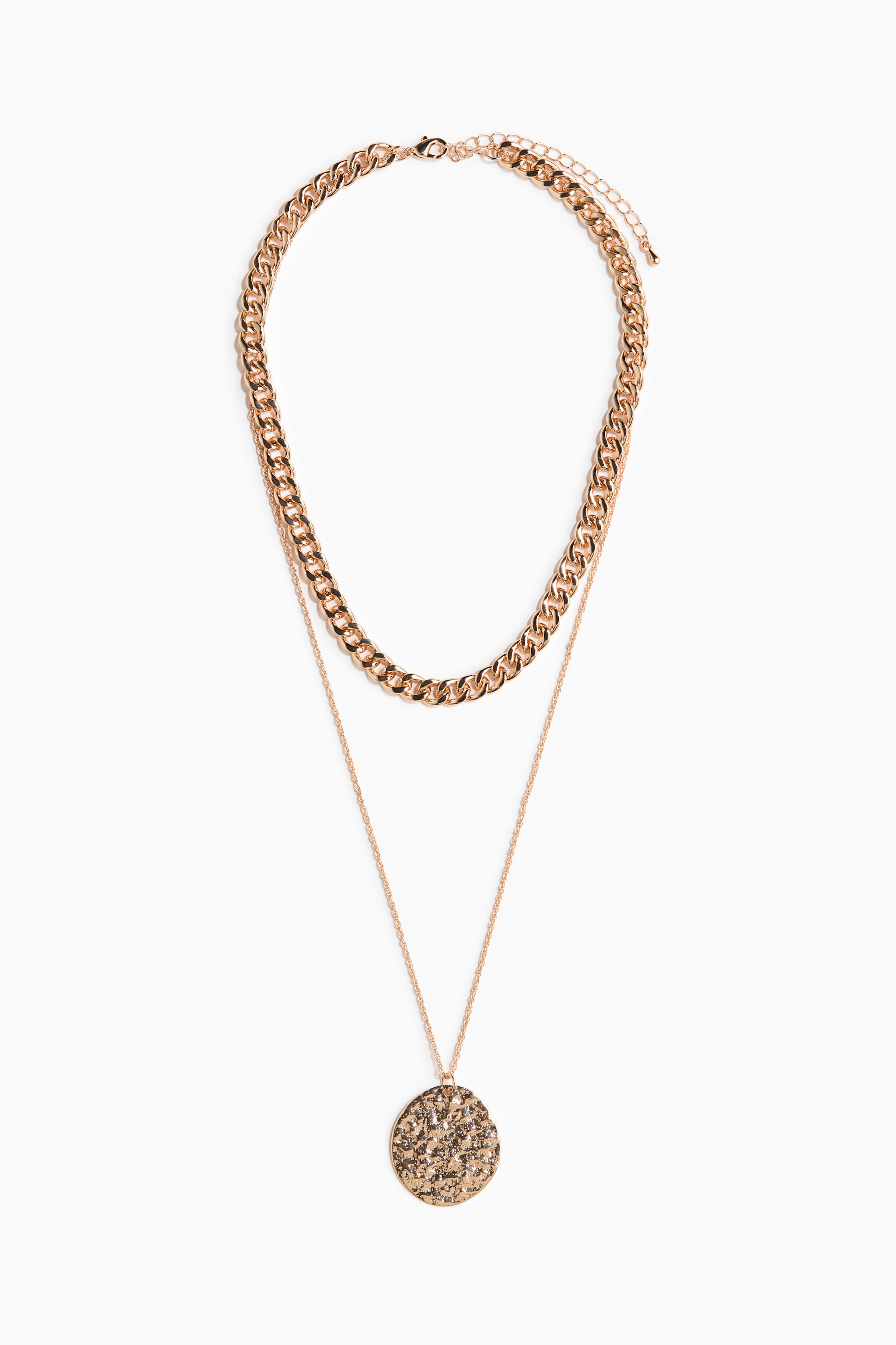 View larger image: A layered necklace featuring a rose gold-toned, thick curb-link chain on the top layer and a thinner chain with a round, textured disc pendant on the bottom layer, complete with a lobster clasp and extender chain visible at the top.
