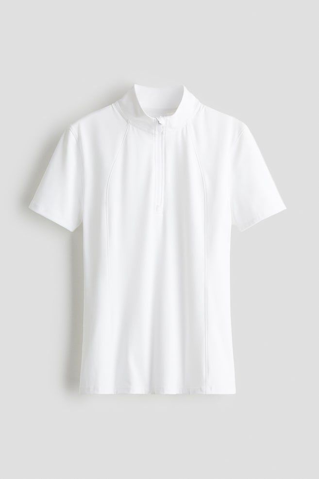 A white short-sleeved top is showing its front, featuring a stand-up collar, a quarter-zip closure, and contoured seams running vertically down the front panels. - 1