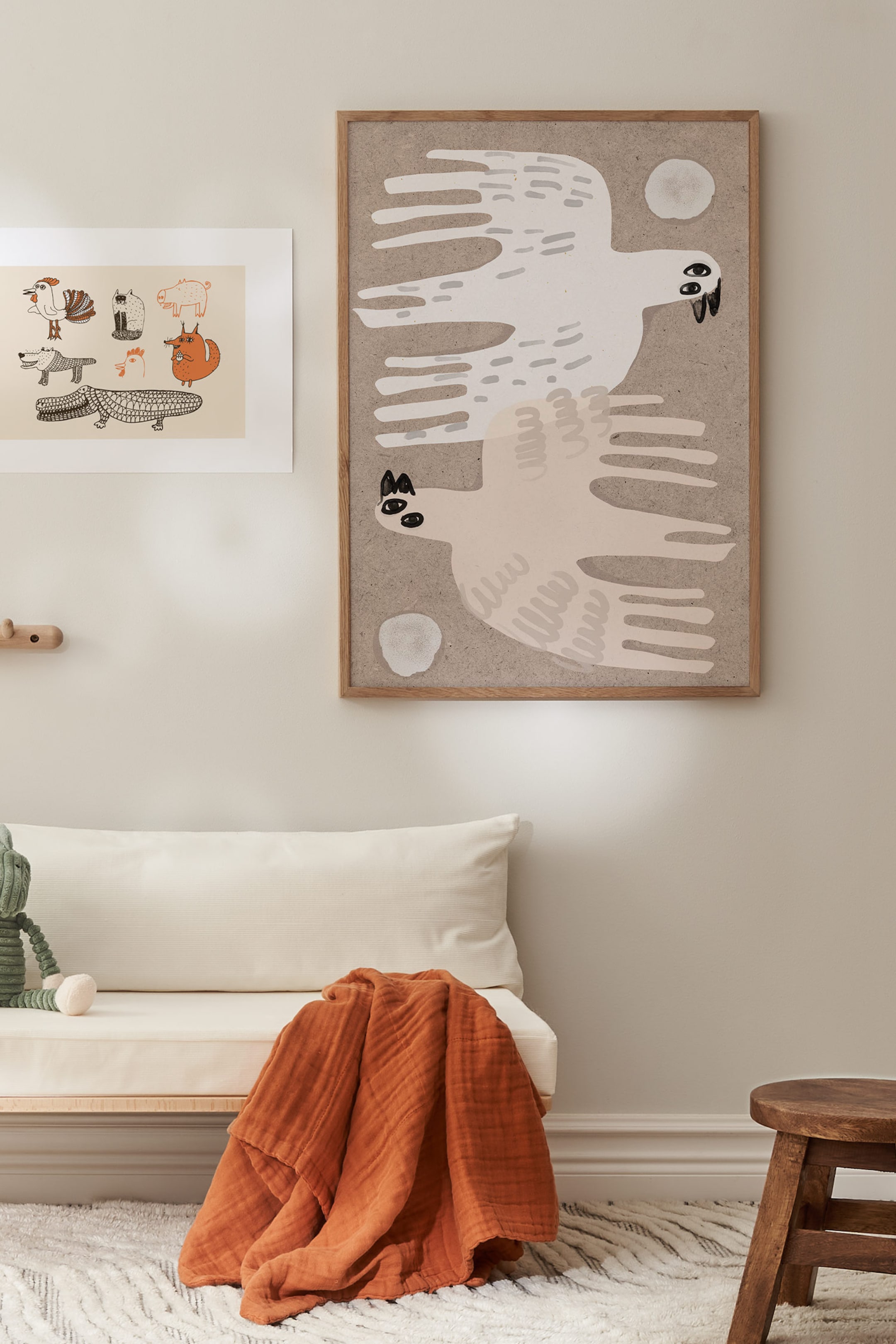Ver imagem maior: Uma impressão artística emoldurada apresenta duas aves estilizadas e abstratas voando horizontalmente em direções opostas sobre um fundo texturizado em castanho-claro. A obra retrata as aves em branco sujo e bege-claro, com penas alongadas, semelhantes a dedos, e olhos simples a preto e branco, tudo enquadrado por uma moldura fina de madeira natural.