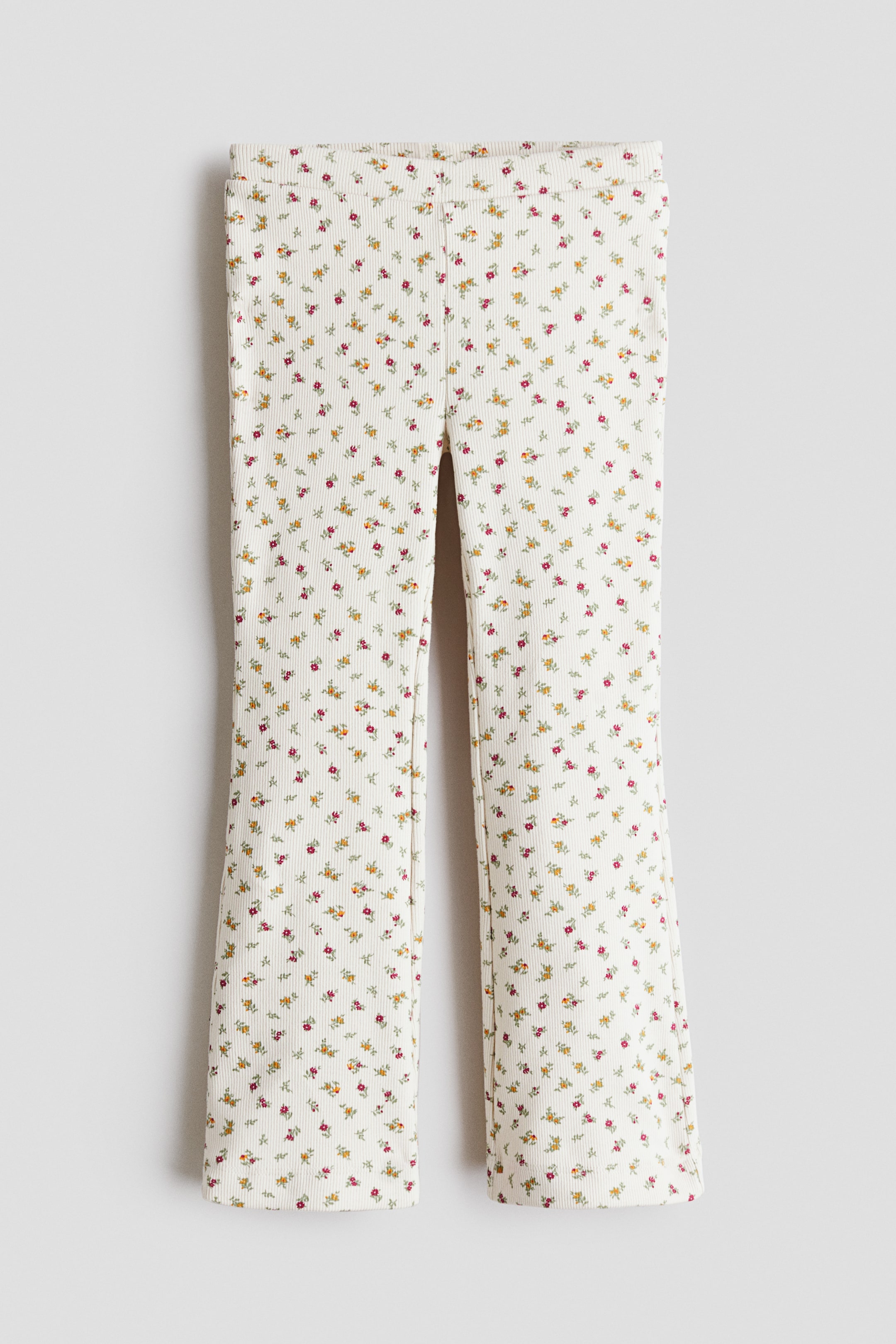 View larger image: The trousers are shown from a front view, laid flat, showcasing a cream ribbed fabric adorned with a pattern of small yellow, orange, and reddish-pink flowers. The legs exhibit a slight flare from the knee down.