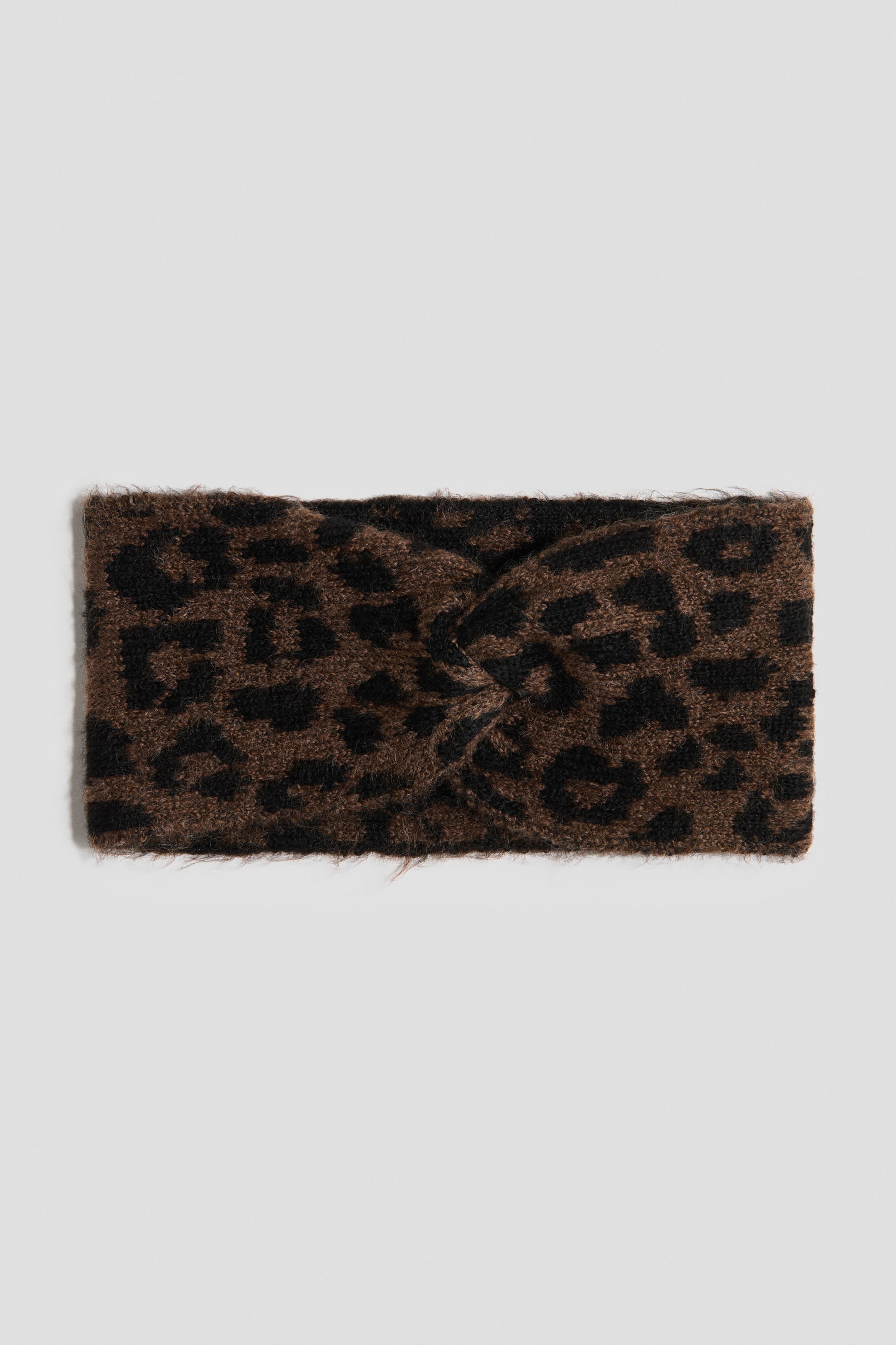View larger image: A double-layered headband is featuring a soft cable knit in a brown and black leopard print, with a decorative twisted detail at the front.