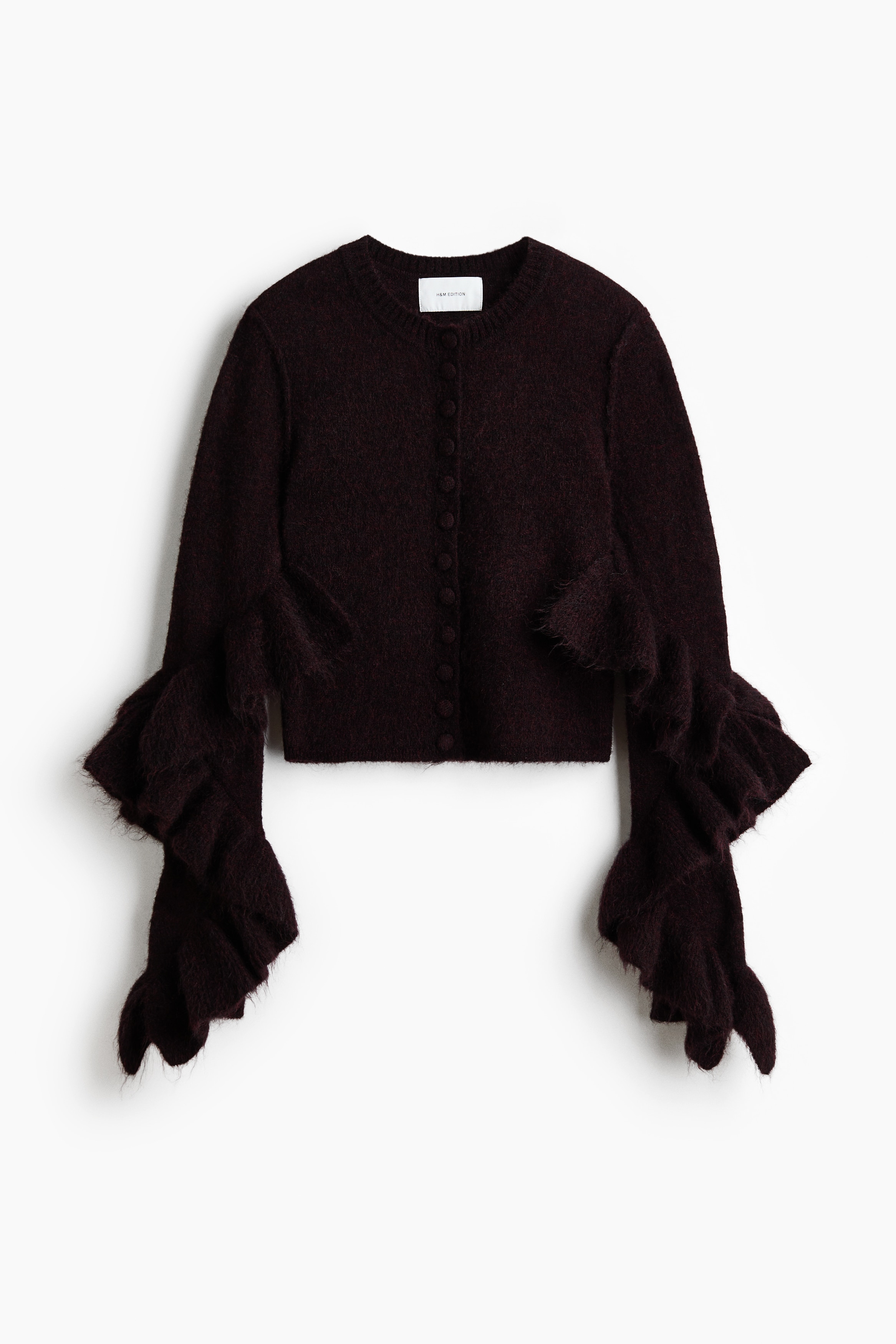 Un cardigan en maille bordeaux foncÃ©, en mÃ©lange de mohair et de laine, est portÃ© par le mannequin, prÃ©sentÃ© de dos. Le cardigan prÃ©sente des volants superposÃ©s spectaculaires sur le bas des manches ainsi quâun ourlet cÃ´telÃ©, et il est associÃ© Ã  une Ã©charpe crÃ¨me drapÃ©e et Ã  un pantalon blanc.