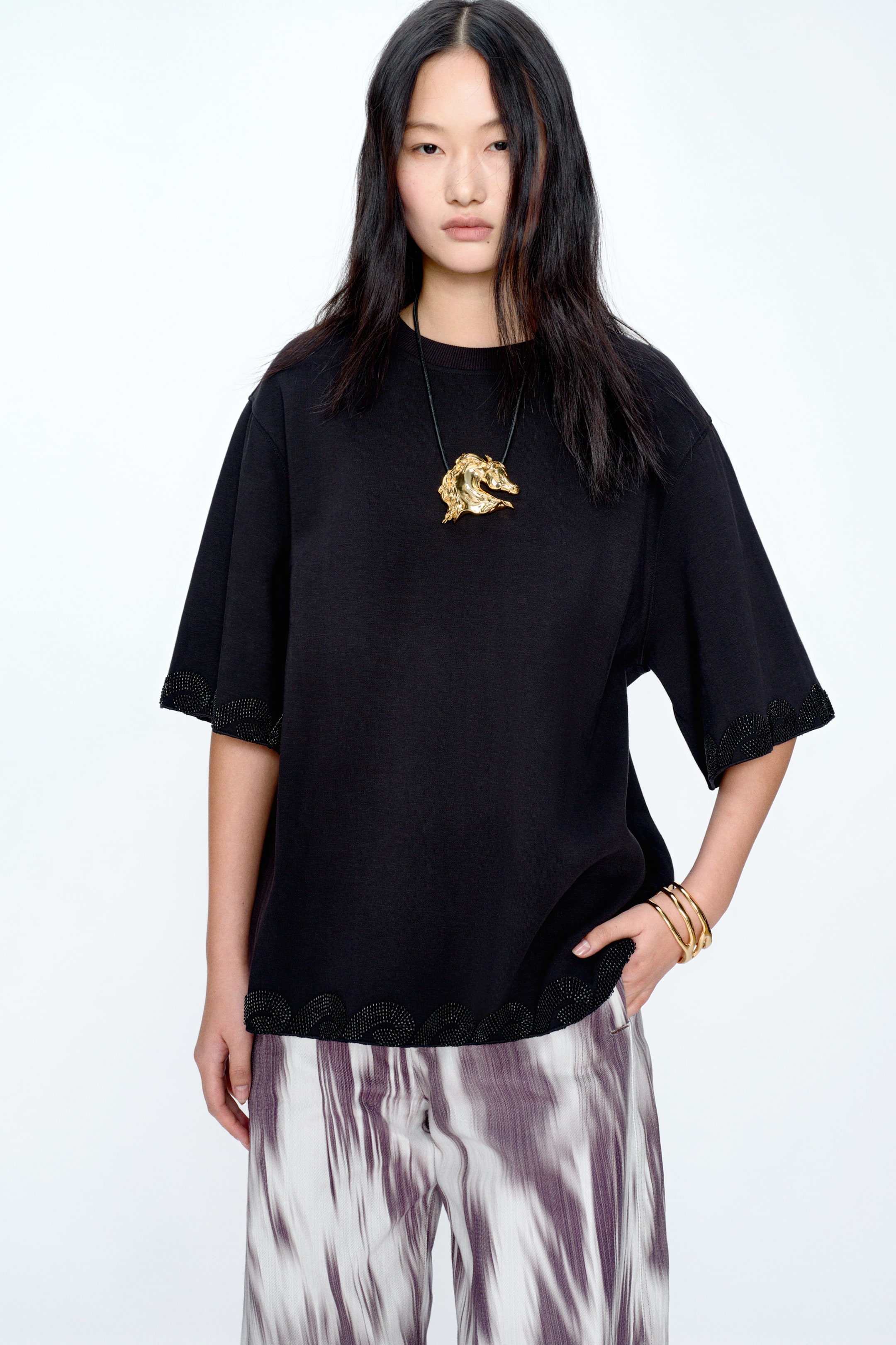 View larger image: A black crew neck top featuring wide, short sleeves. The scalloped hem and sleeve openings are embellished with intricate black beadwork.