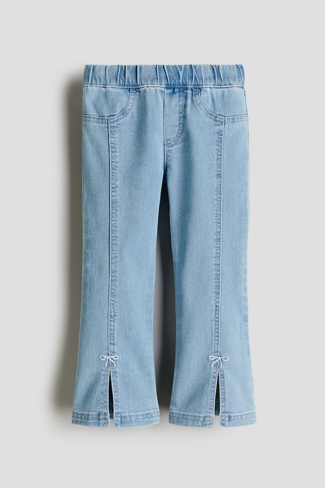 Front-facing light blue stretchy denim jeggings are presenting an elasticated waist, a stitched fake fly, and faux front pockets. The legs are finishing with flared hems that are featuring an embroidered bow detail and a front slit. - 1
