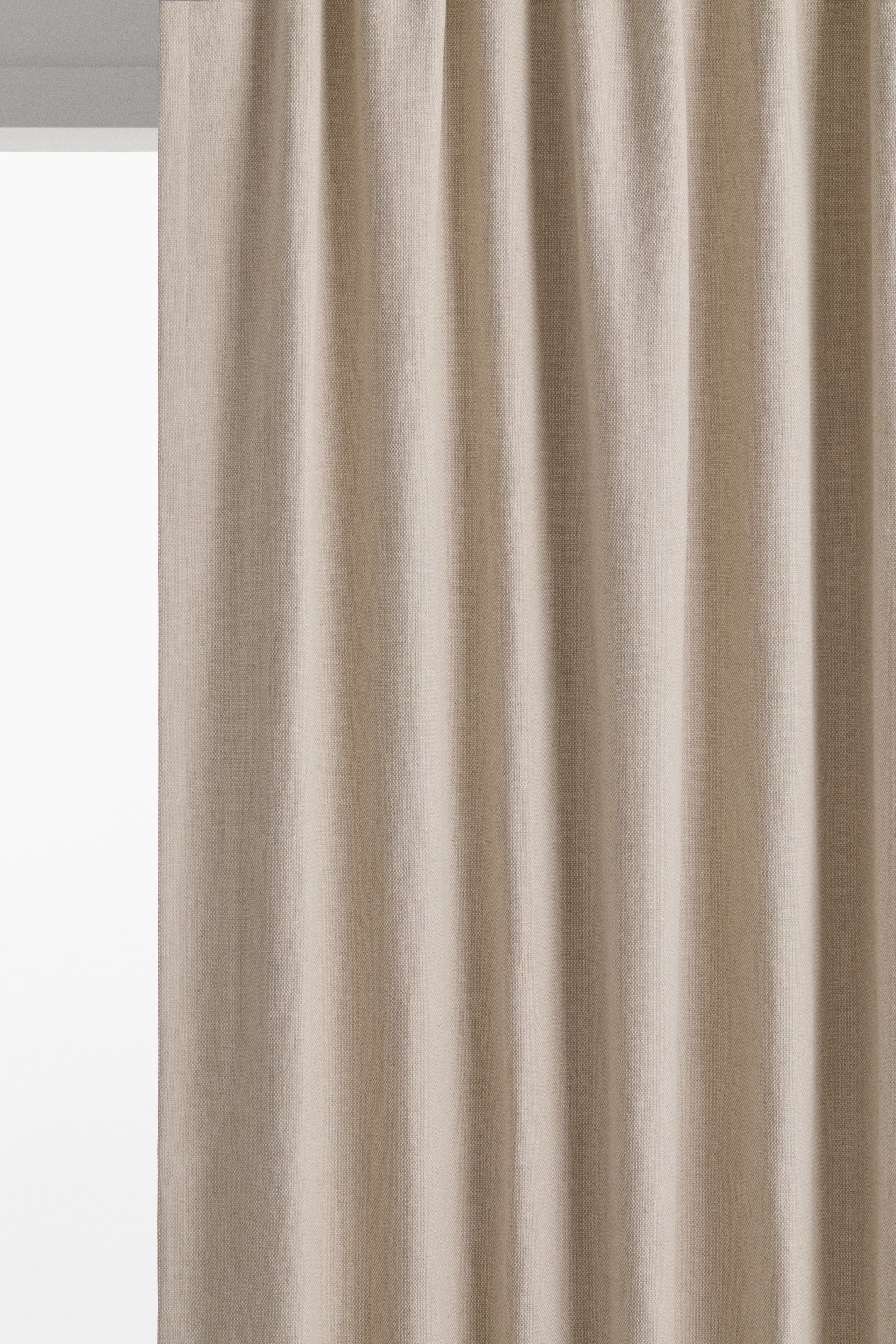 Visualizza immagine più grande: Una tenda color beige chiaro è appesa, formando morbide pieghe verticali dal bordo superiore raccolto. Il tessuto presenta una sottile trama intrecciata.