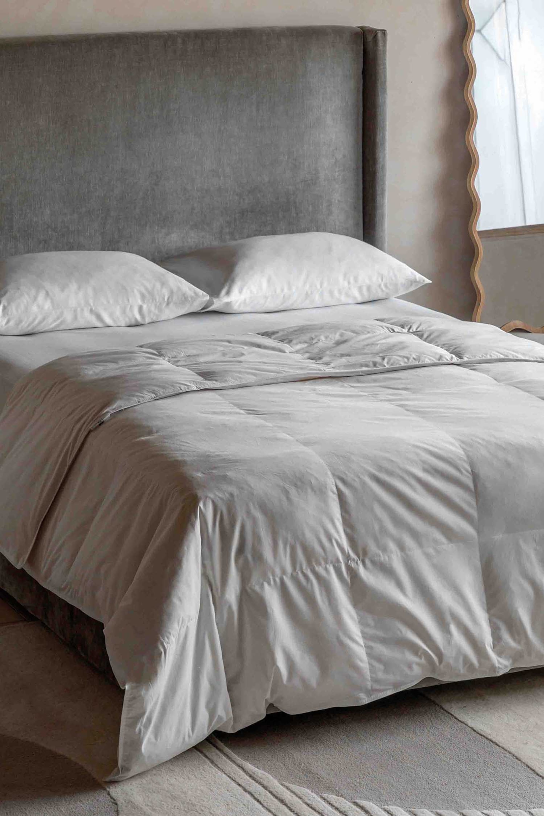 View larger image: A white duvet is laid across a bed, viewed from a front-right angle. It features square baffle quilting and a soft texture, with two white pillows placed at the head of the bed beneath its folded-back section.