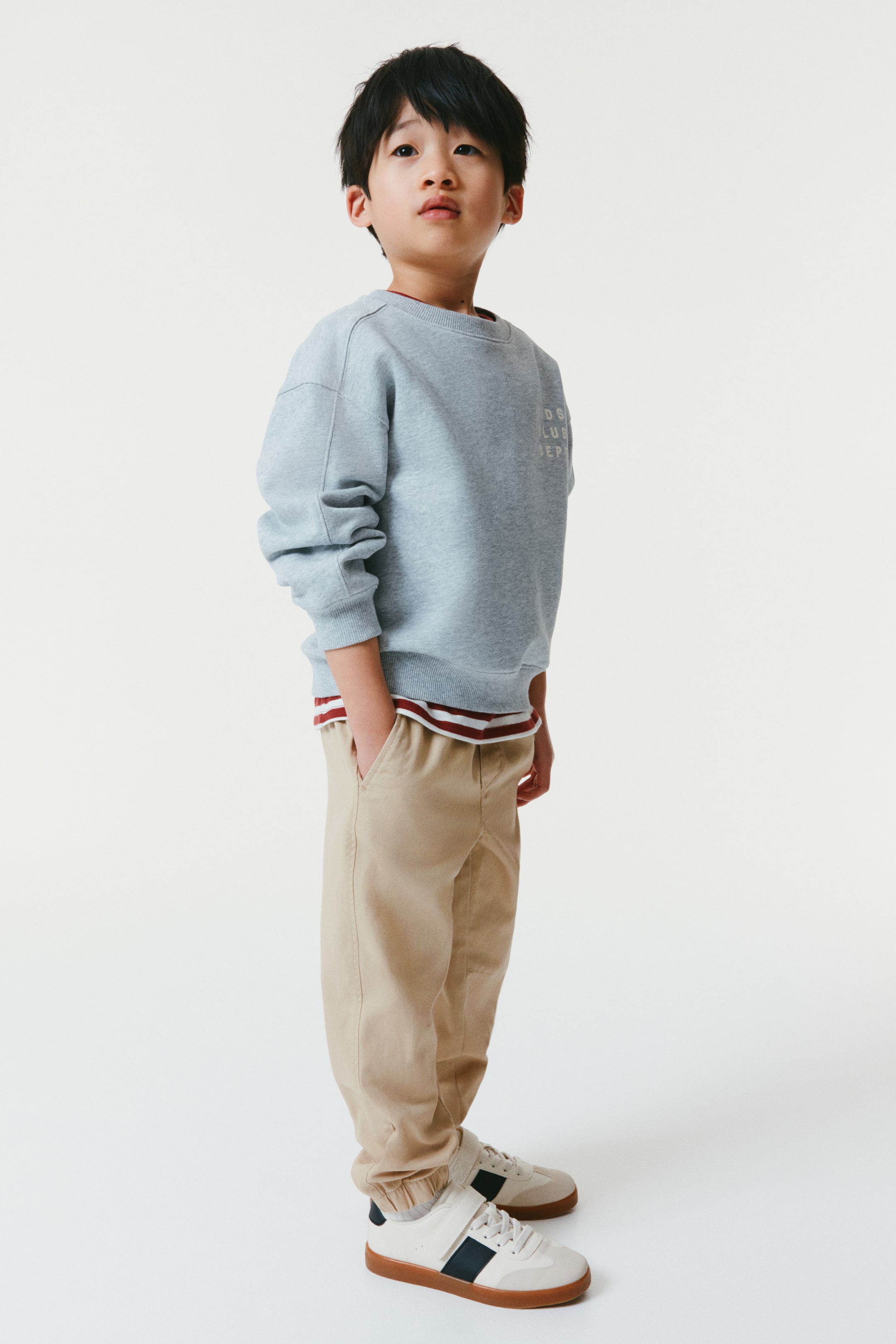 Visa större bild: Khaki bomullstwill-joggers har en elastisk midja med dragsko, en fejkad gylf och sidofickor, sett framifrån. De är designade med raka ben, veck vid knäna och täckt elastik vid fållarna.