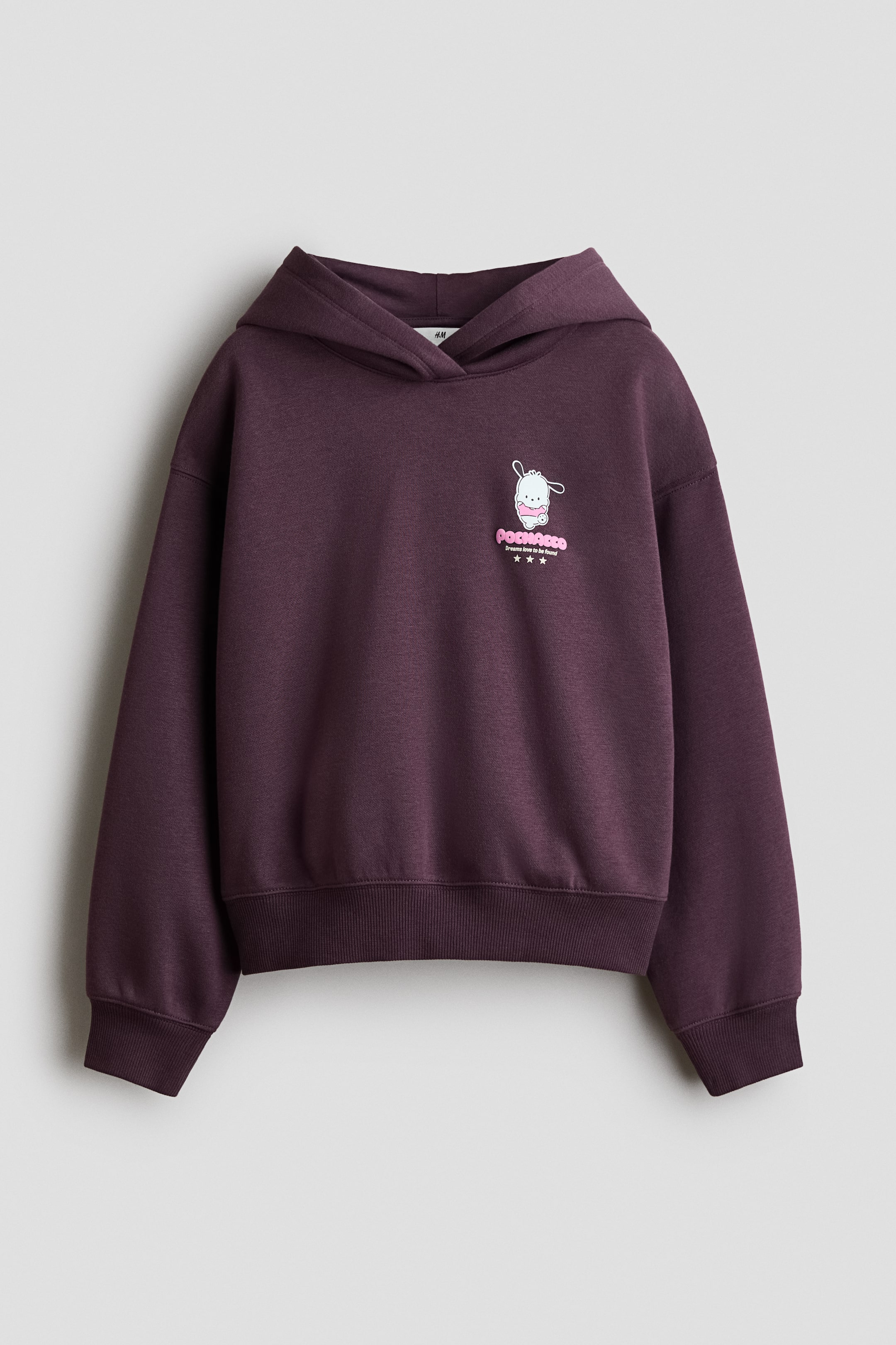 View larger image: A dark purple loose-fit hoodie is shown from the front, featuring a white cartoon character print with pink text reading "POCHACCO Dreams love to be found!" and three stars. The hoodie is designed with a jersey-lined hood, wrapover front, dropped shoulders, long sleeves, and ribbed cuffs and hem.