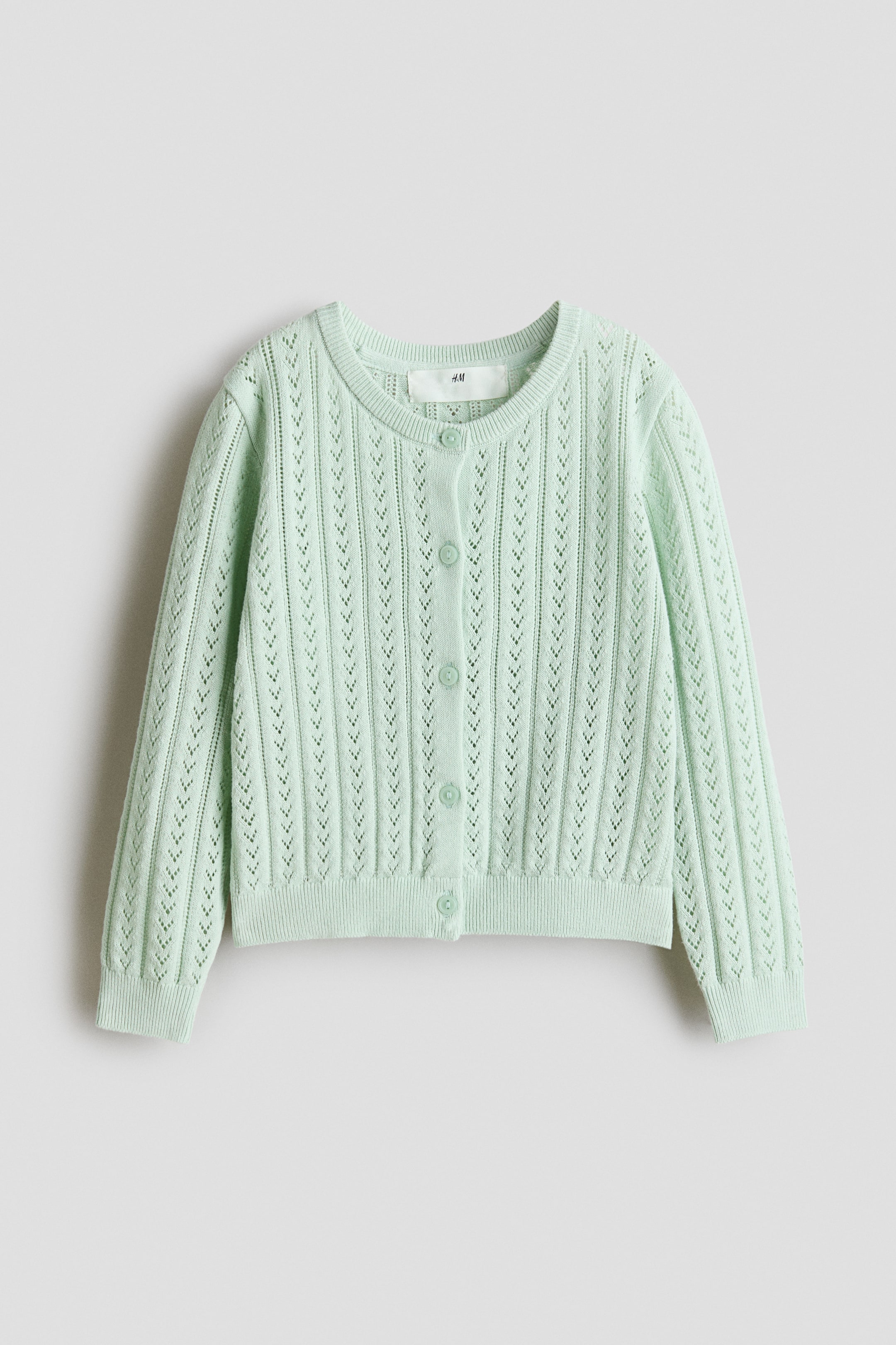 View larger image: A light green cardigan is displayed from the front. It features a soft pointelle-knit cotton fabric with vertical openwork patterns, a round, ribbed neckline, buttons down the front, and ribbing at the cuffs and hem.