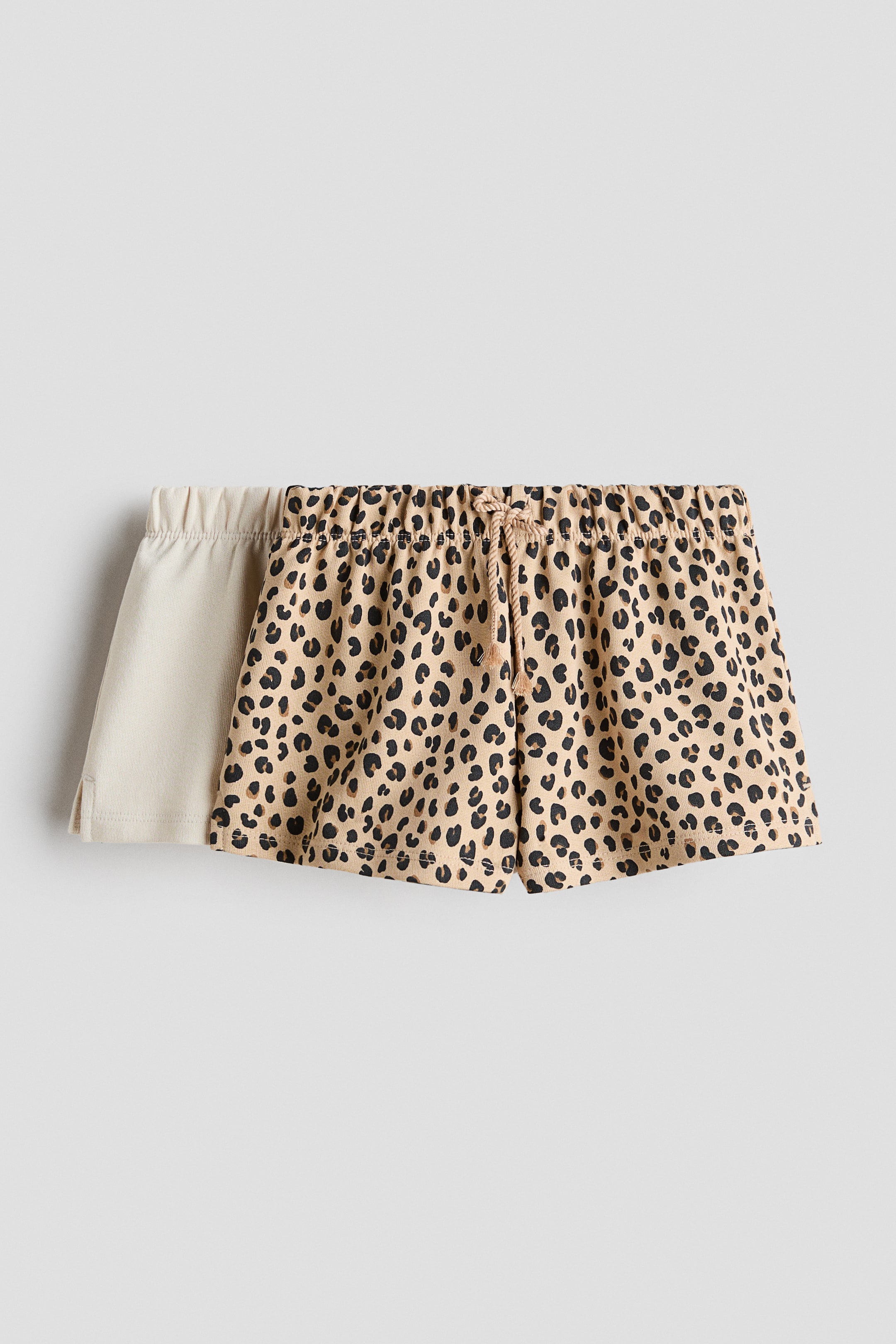 View larger image: "Dalawang pares ng shorts ang nakadisplay sa harap na view. Ang harapang pares ay may leopard print na may elasticated na baywang at may braided na drawstring tie, habang ang pangalawang pares, na bahagyang nakikita sa likuran, ay solidong light beige na may elasticated na baywang at maliit na side vent."