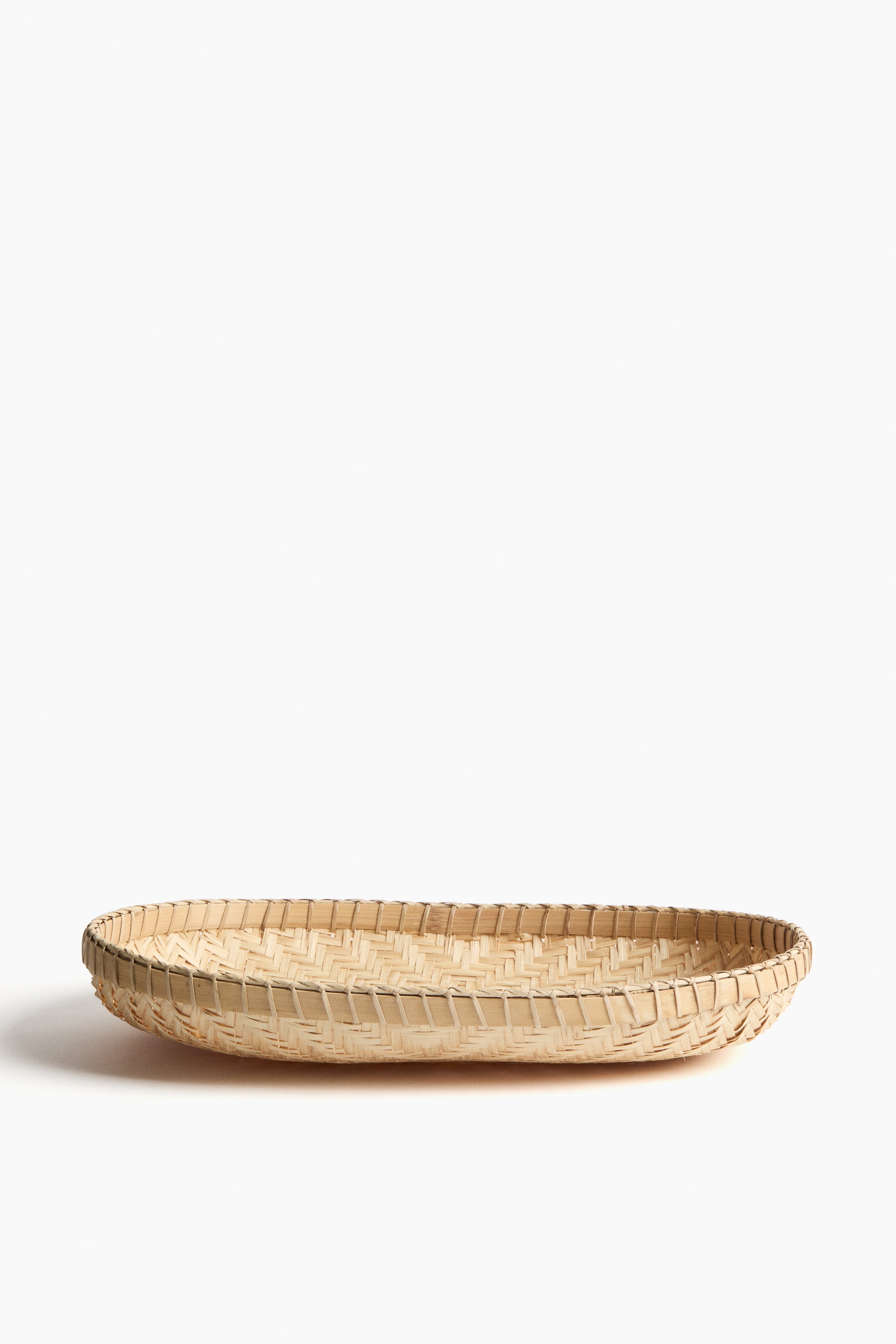 View larger image: A shallow, oval-shaped basket made of light natural bamboo is shown from the front. The base displays a herringbone weave pattern, and the rim features a tightly bound edge.