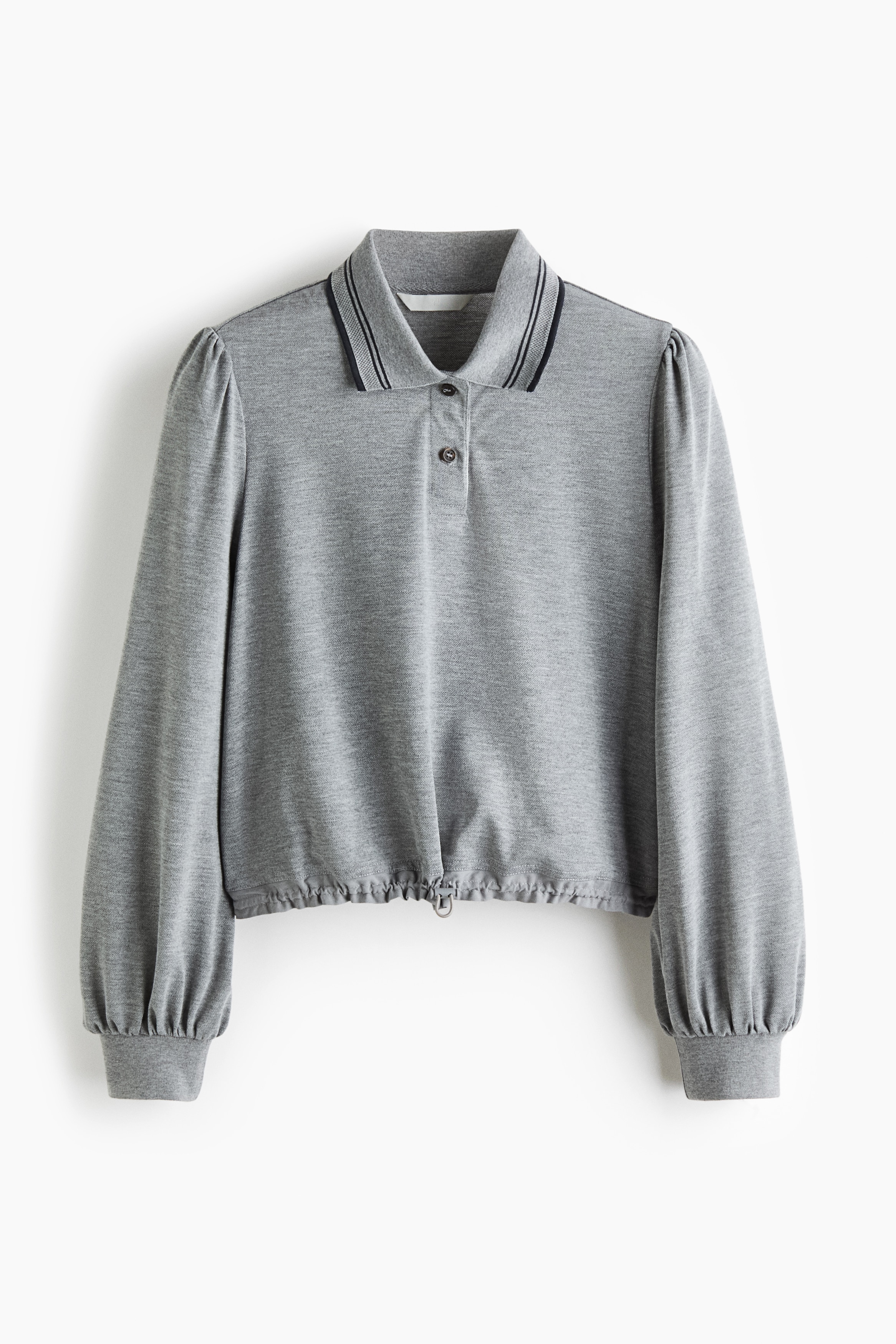 The model is wearing a long-sleeved jersey polo shirt featuring a ribbed collar with contrast tipping, a button placket, and puff sleeves with ribbed cuffs. The shirt is gathered at the waist with an elasticated drawstring and cord stopper, and is styled with dark trousers.