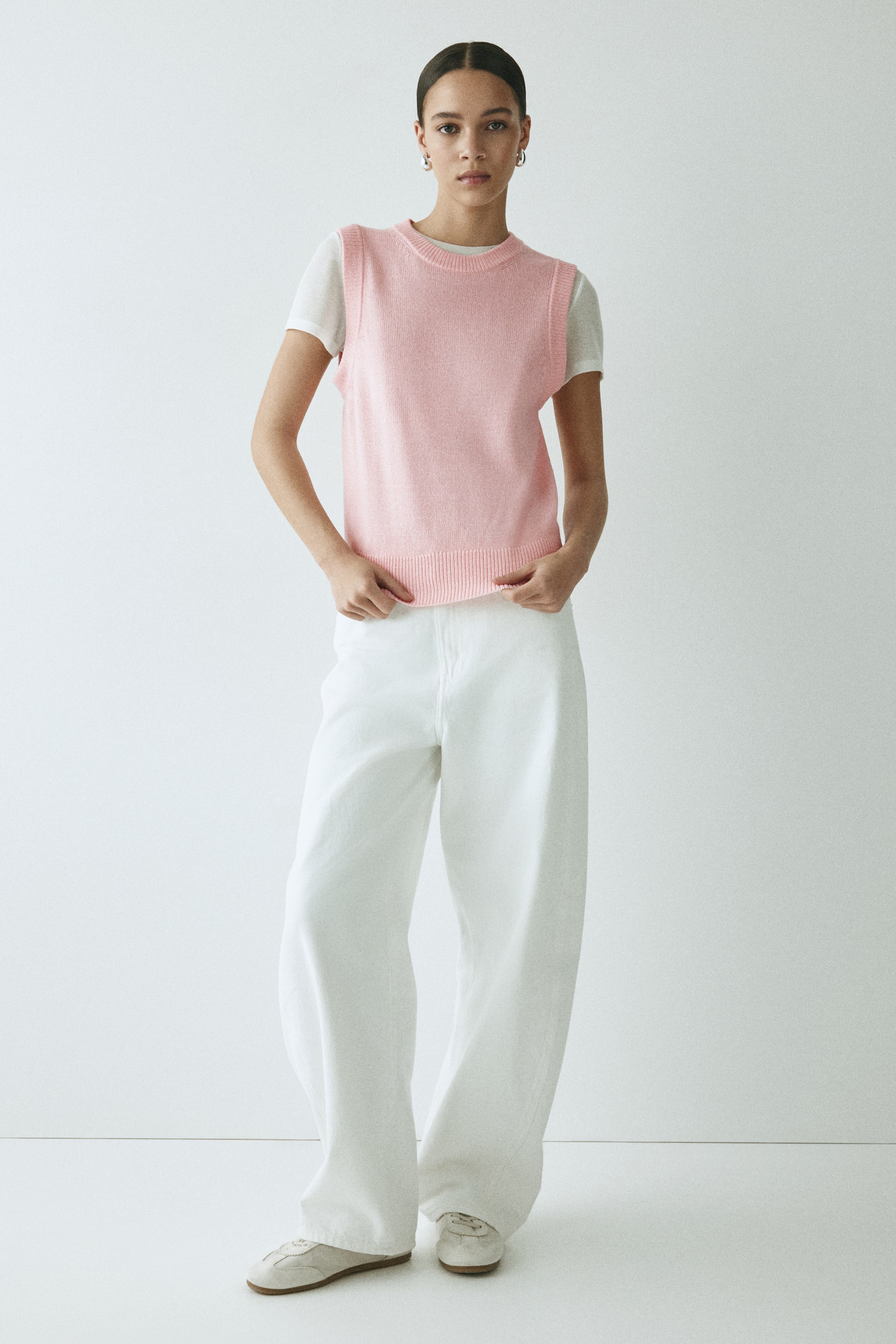 View larger image: A pink knitted vest is worn over a white T-shirt, featuring a crew neck and a ribbed hem.
