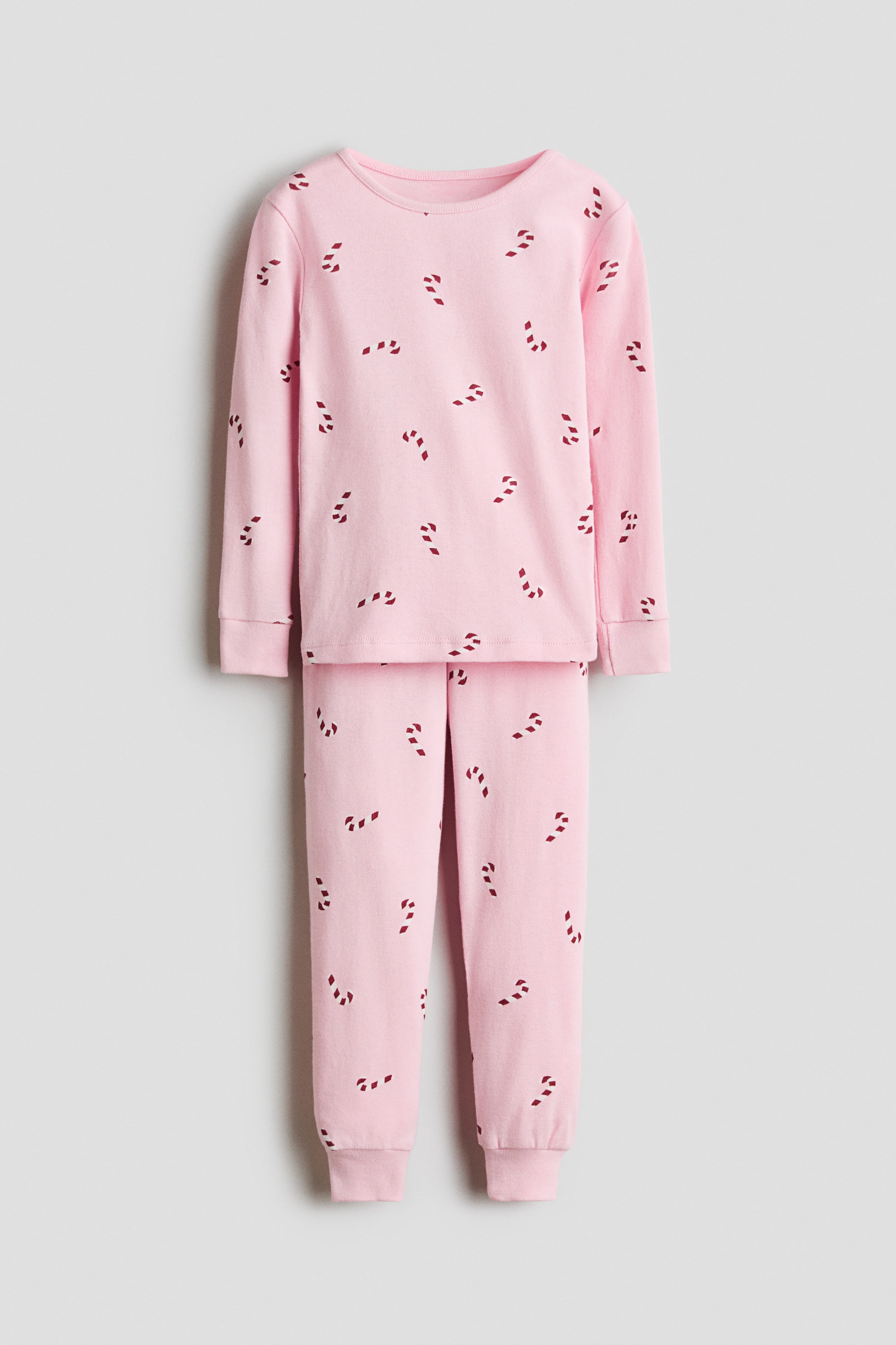 Voir une image plus grande: Une vue de face met en valeur un ensemble de pyjama en coton rose pâle présentant un imprimé intégral de cannes de bonbon rouges. L’ensemble comprend un haut à manches longues avec un col rond et des poignets côtelés, assorti à un pantalon coordonné qui se resserre vers des ourlets côtelés.