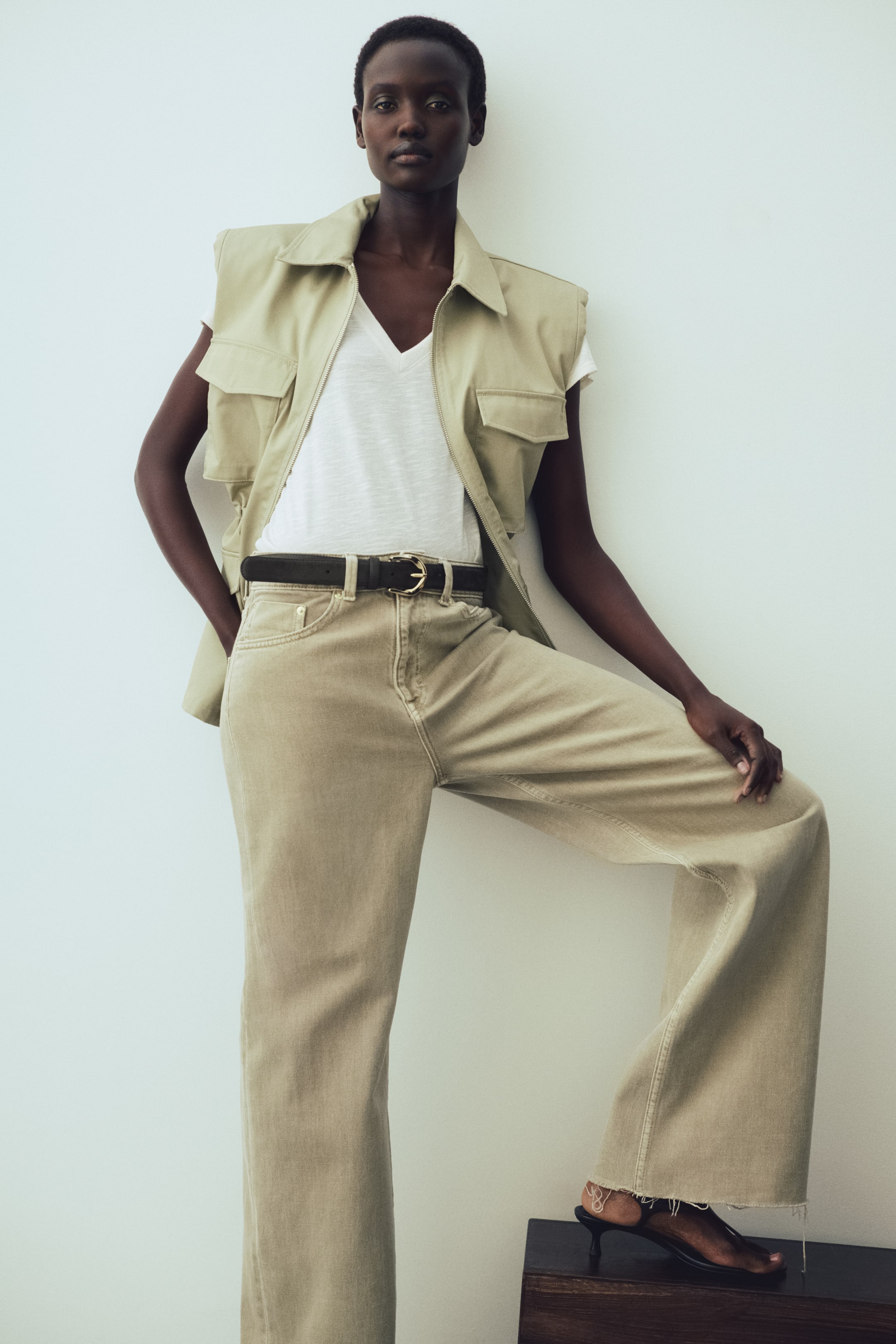 View larger image: The model is wearing a white T-shirt crafted from slub jersey. It boasts a deep V-neckline accentuated by a narrow trim and is stylishly layered beneath a light-coloured vest.