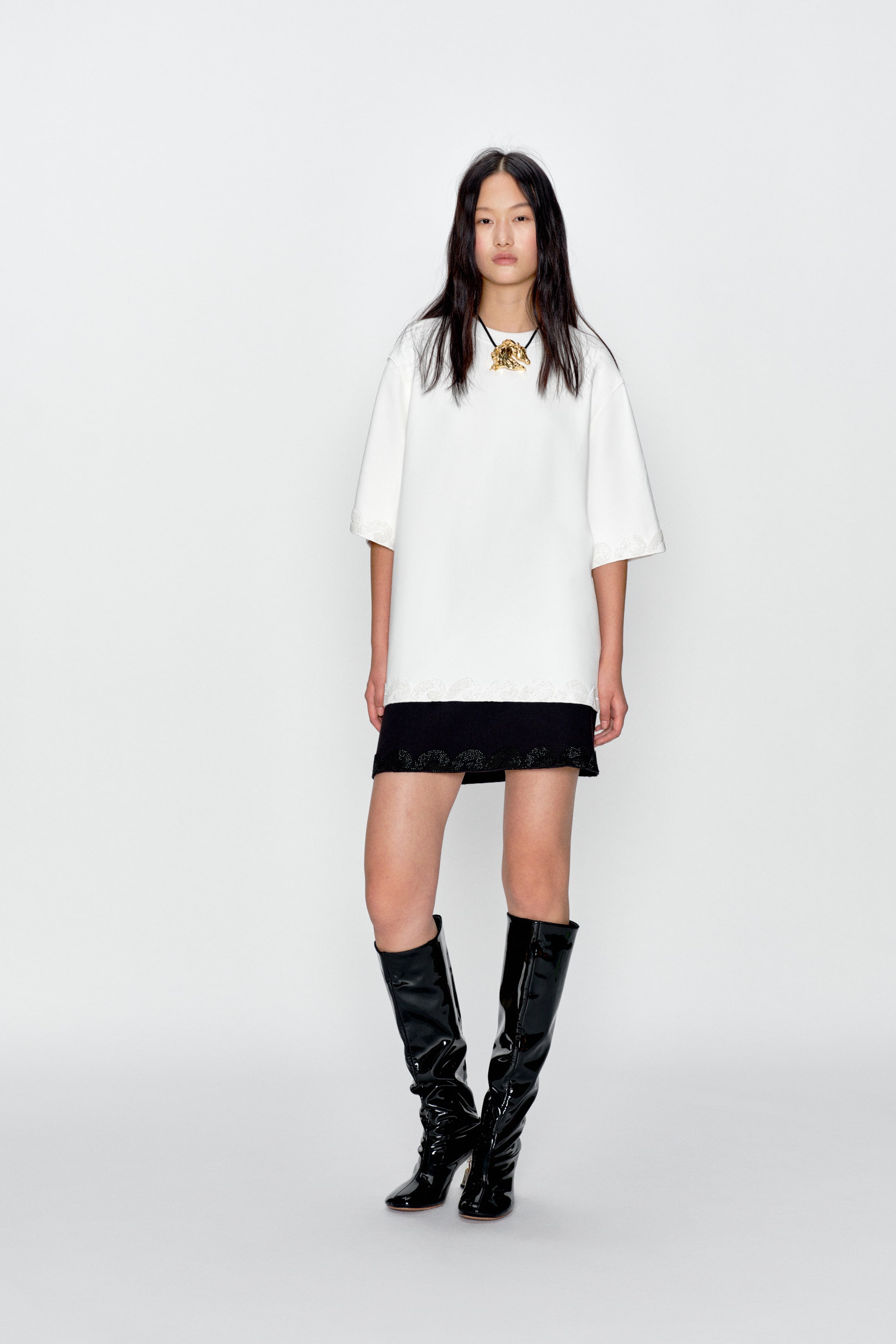 View larger image: A white tunic top featuring a relaxed fit, short sleeves, and white lace trim along the sleeve cuffs and bottom hem. A black mini skirt can be seen under the top, showcasing black embroidered lace along its hem.