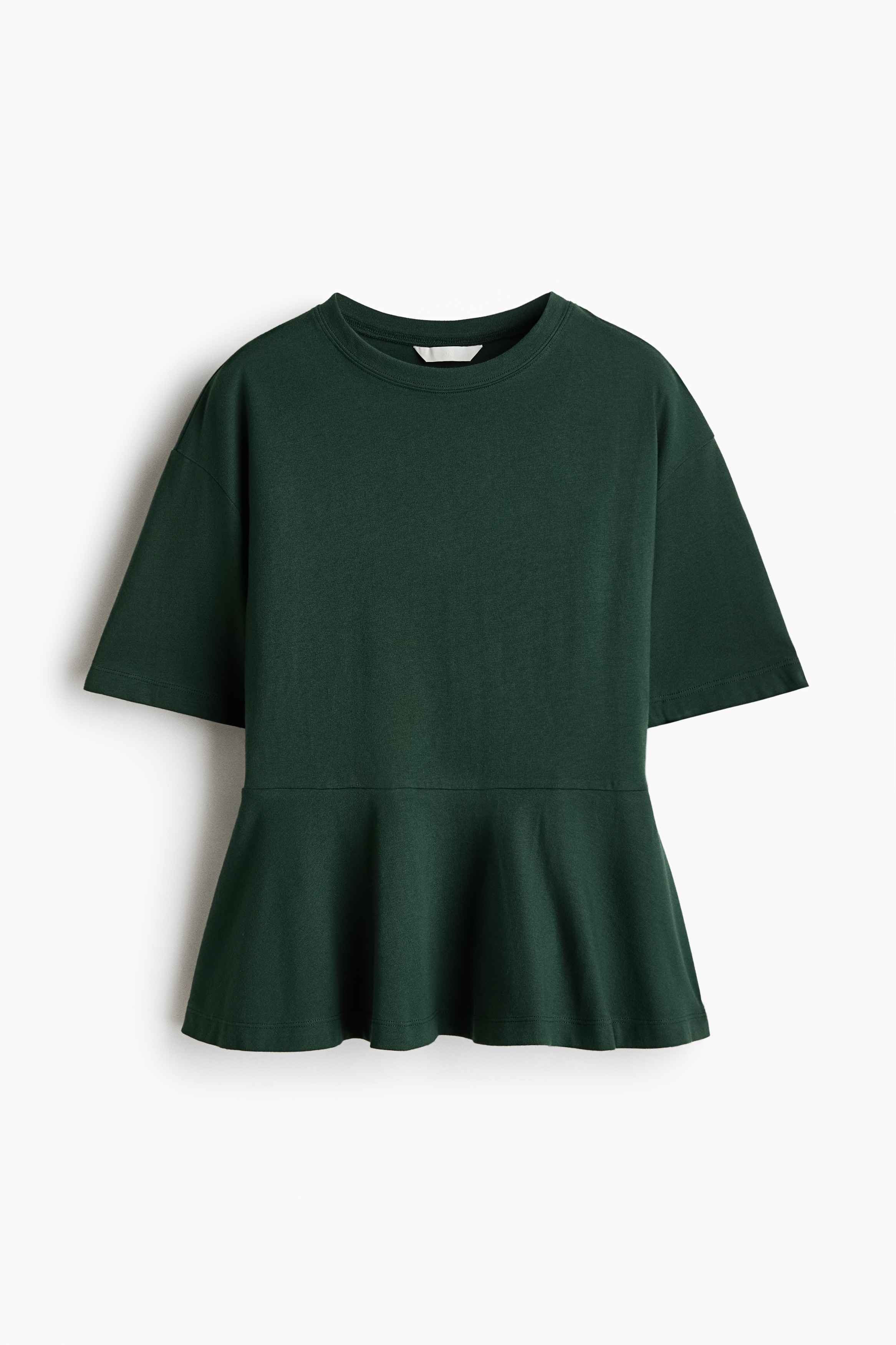 A dark green cotton jersey top featuring a round rib-trimmed neckline, dropped shoulders, short sleeves, and a flared peplum is being worn by the model. The top is styled with black leather shorts, a gold pendant necklace, and tall black boots.