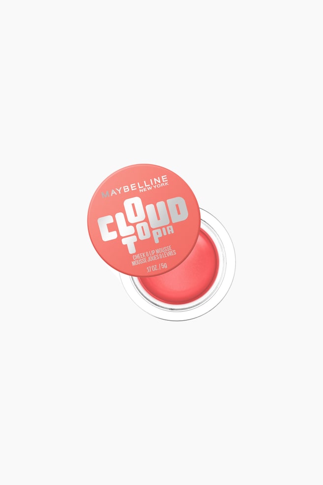 En Maybelline Cloud Topia Cheek & Lip Mousse i en åben, rund og gennemsigtig krukke ses ovenfra i en let skrå vinkel. Den glatte, koralfarvede mousse er synlig indeni, mens det koralfarvede låg med sølvskriften 'MAYBELLINE NEW YORK' og 'CLOUD TOPIA' hviler let på klem og viser produktoplysninger som 'CHEEK & LIP MOUSSE' og '.17 OZ. / 5G'. - 1