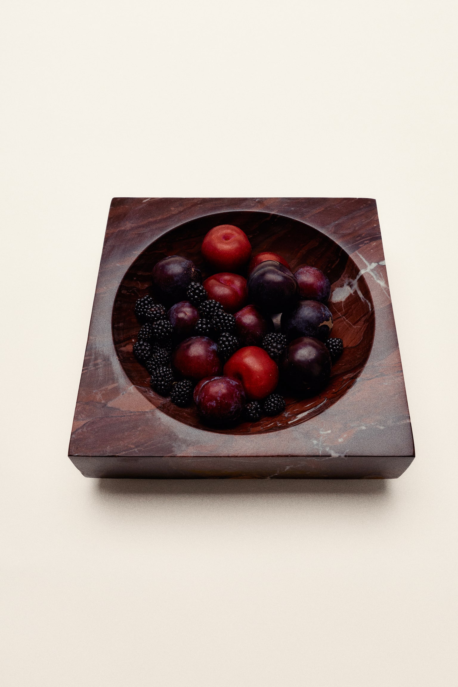 Une pièce rectangulaire solide en marbre rouge foncé est légèrement orientée vers la droite, exhibant sa surface polie avec des veines blanches et rouge plus clair, et présentant une indentation centrale arrondie formant un bol peu profond. - 1