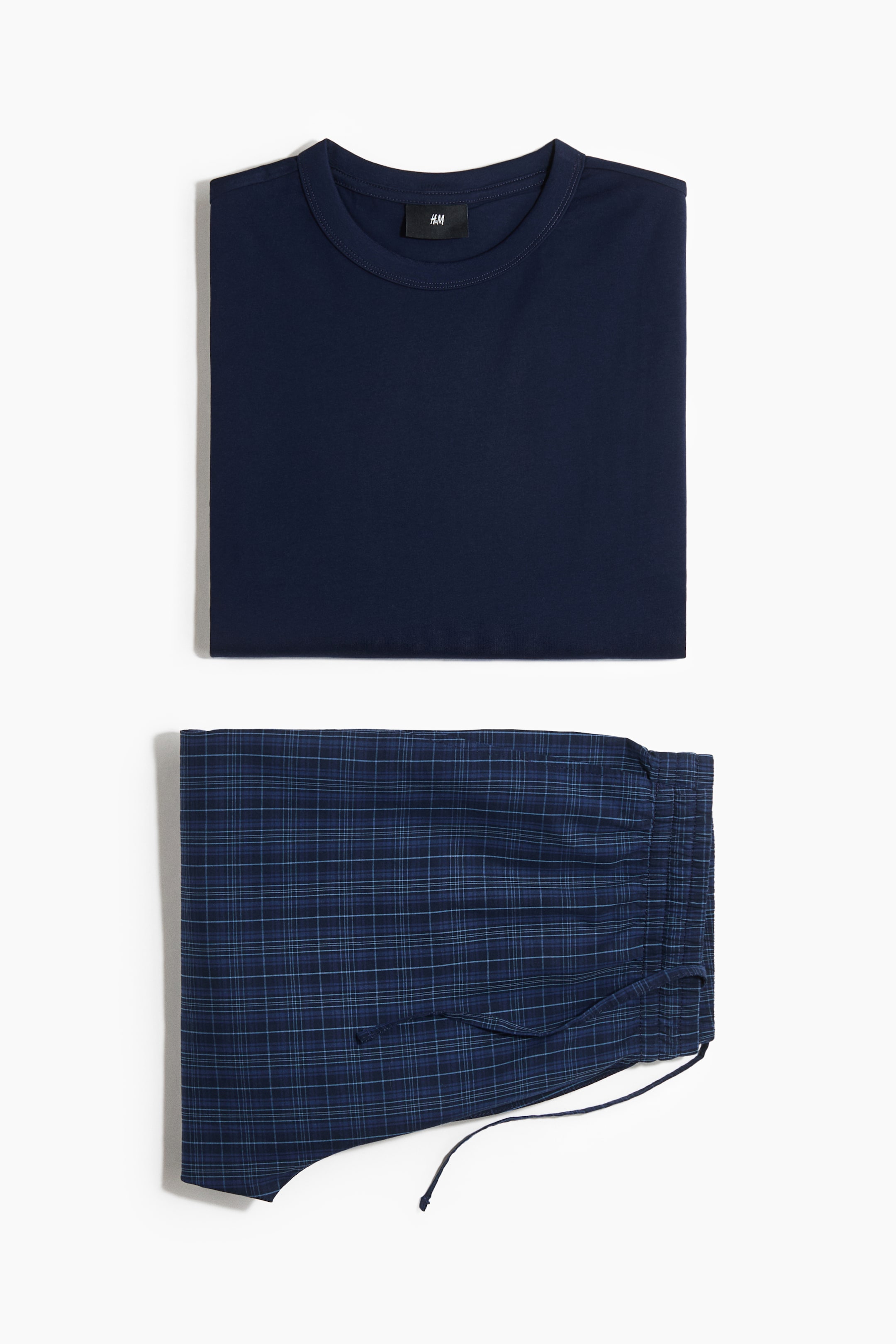 View larger image: A navy blue t-shirt is neatly folded, displaying its ribbed crew neck and a black H&M label. Below it, a pair of dark blue plaid pants is folded, showing a drawstring at the elasticated waist.