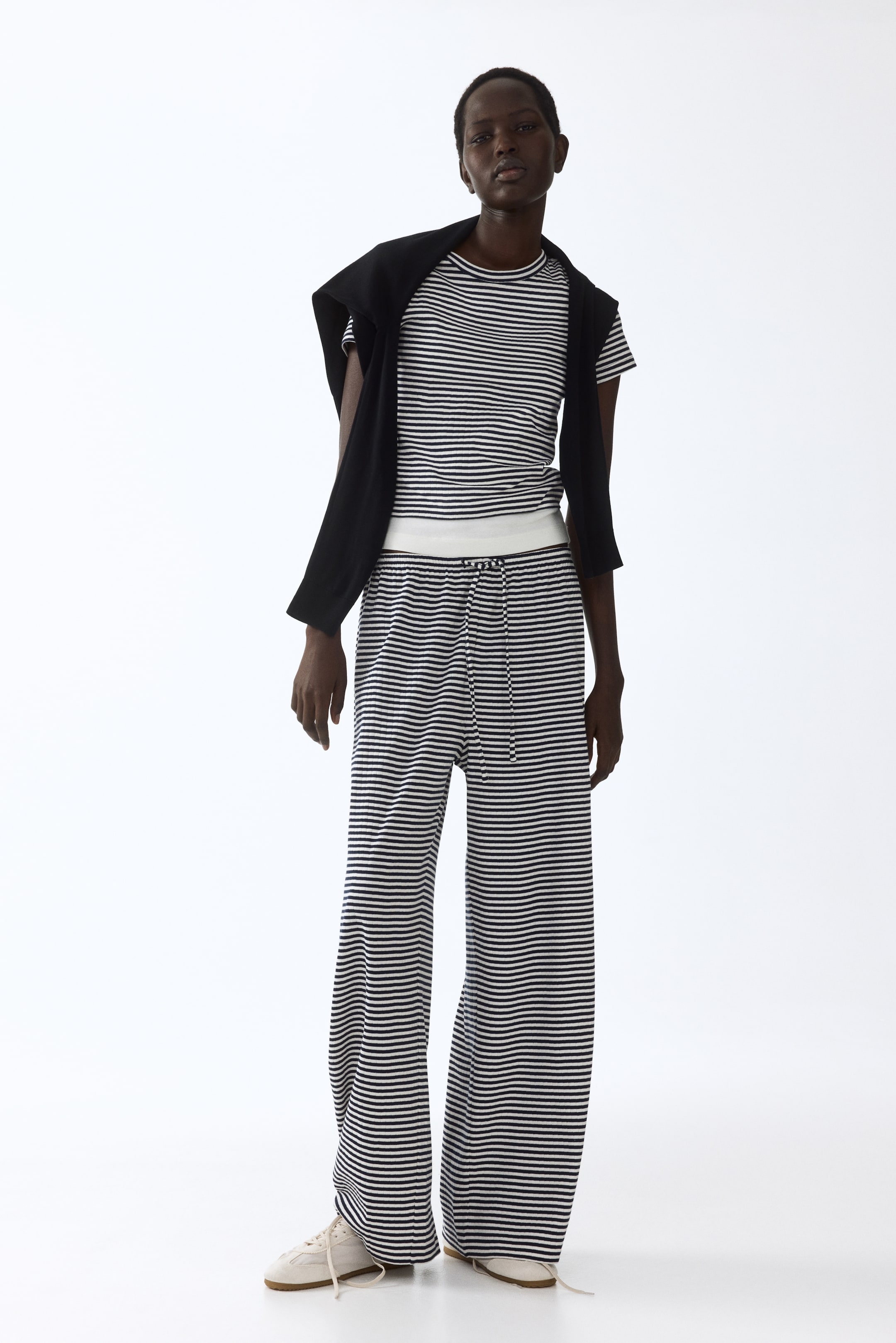 View larger image: A short-sleeve t-shirt and wide-leg pants feature horizontal black and white stripes. The t-shirt has a crew neck, while the pants showcase a drawstring waist with a visible white elastic waistband, complemented by a black garment draped over the shoulders.