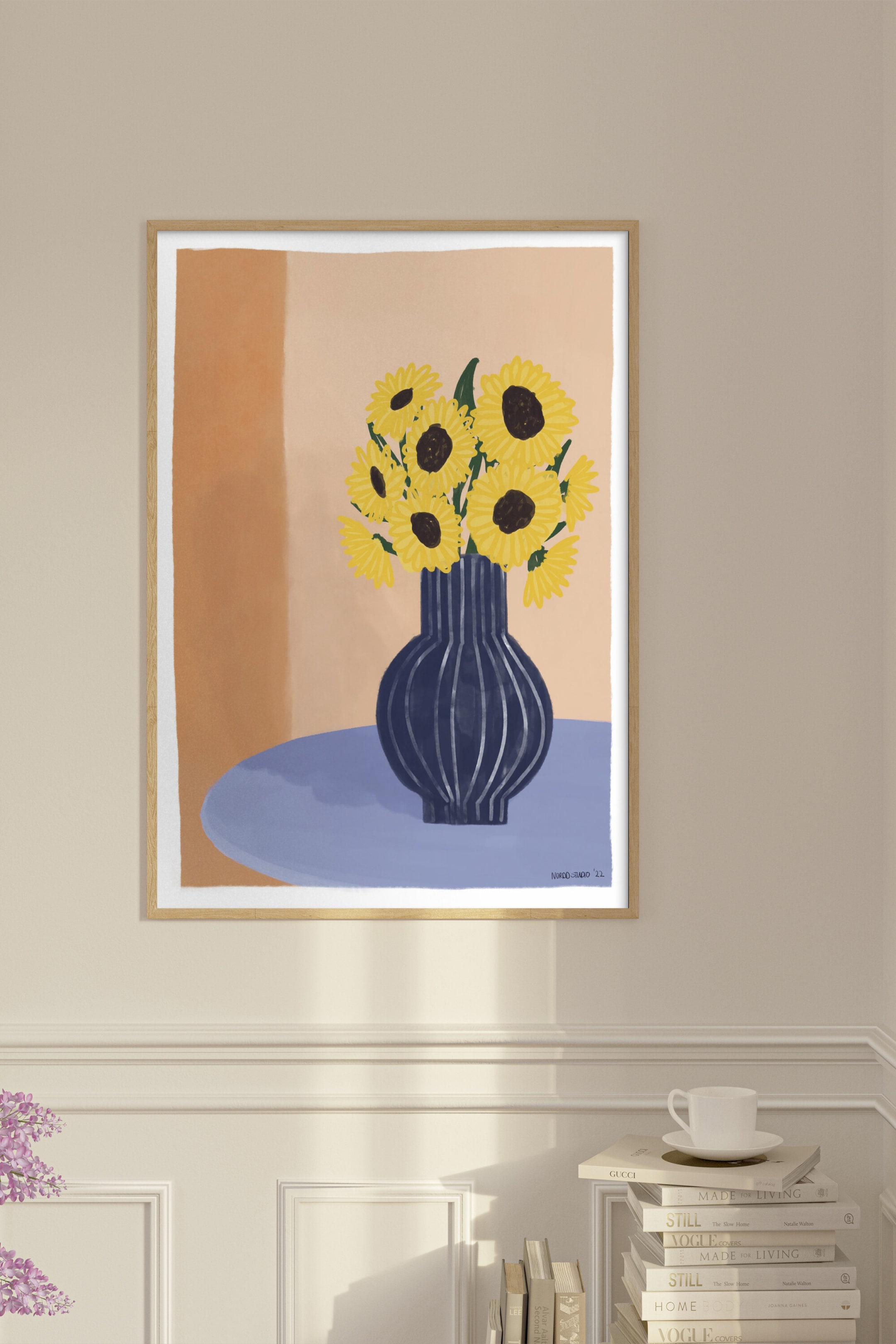 Grotere afbeelding bekijken: De ingelijste kunstdruk toont een illustratie van gele zonnebloemen met donkere harten in een donkerblauwe gestreepte vaas, rustend op een lichtblauw oppervlak, en is ingesloten in een dunne, natuurlijke houten lijst met een witte rand.