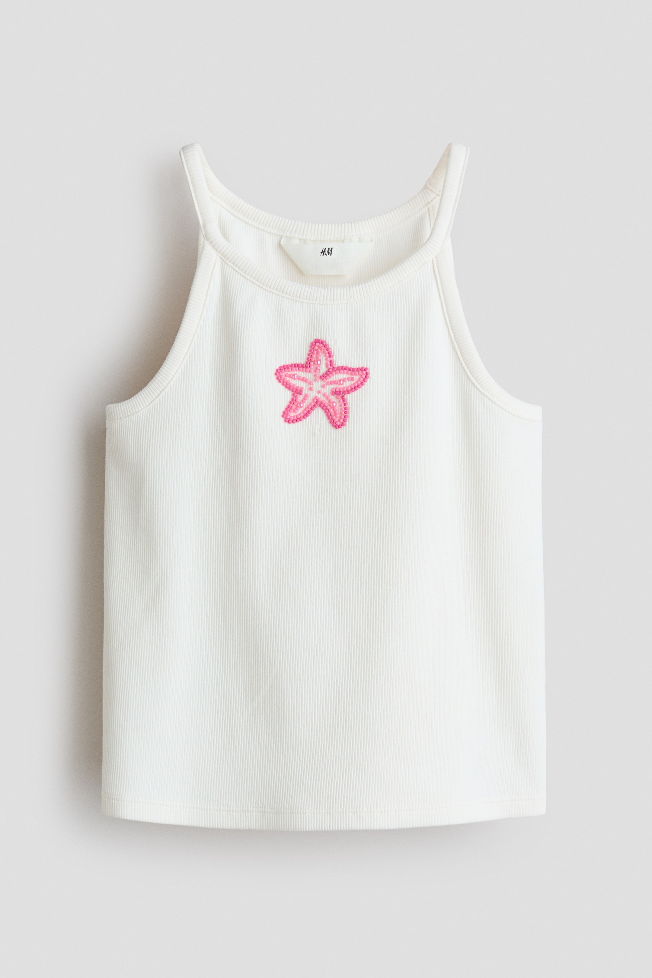 View larger image: An off-white ribbed knit tank top is facing front, showcasing a rounded neckline and slender straps. A centrally placed pink beaded starfish design embellishes the front.